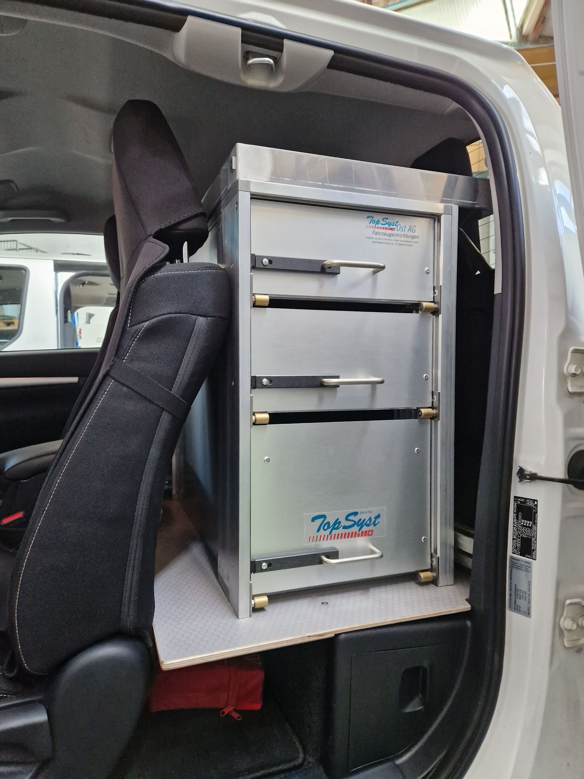 Aluminium-Schubladen in der offenen Fahrzeugtür. Neben den Schubladen befinden sich ein schwarzer Sitz und eine schwarze Box.