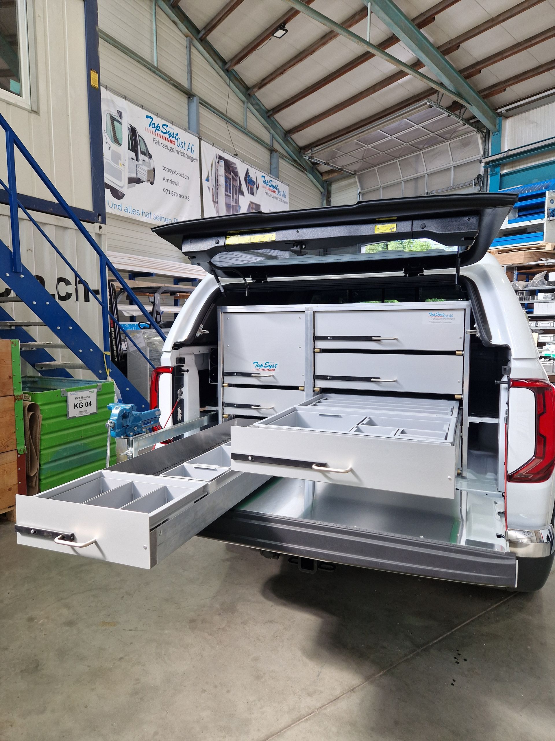 Weißer LKW mit ausgefahrenen hinteren Schubladen, der geordnete Werkzeuge in einer Werkstattumgebung präsentiert.