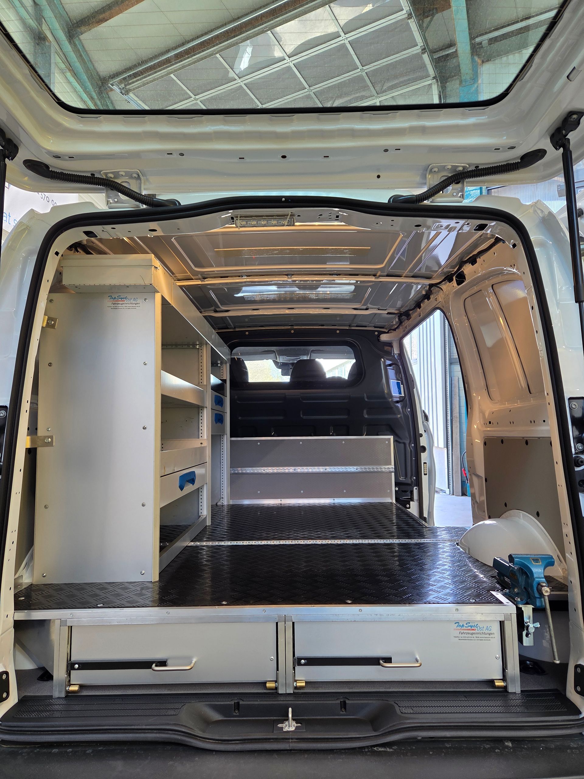 Innenraum eines weißen Lieferwagens mit Regalen, Schubladen und einem Metallboden zur Lagerung.