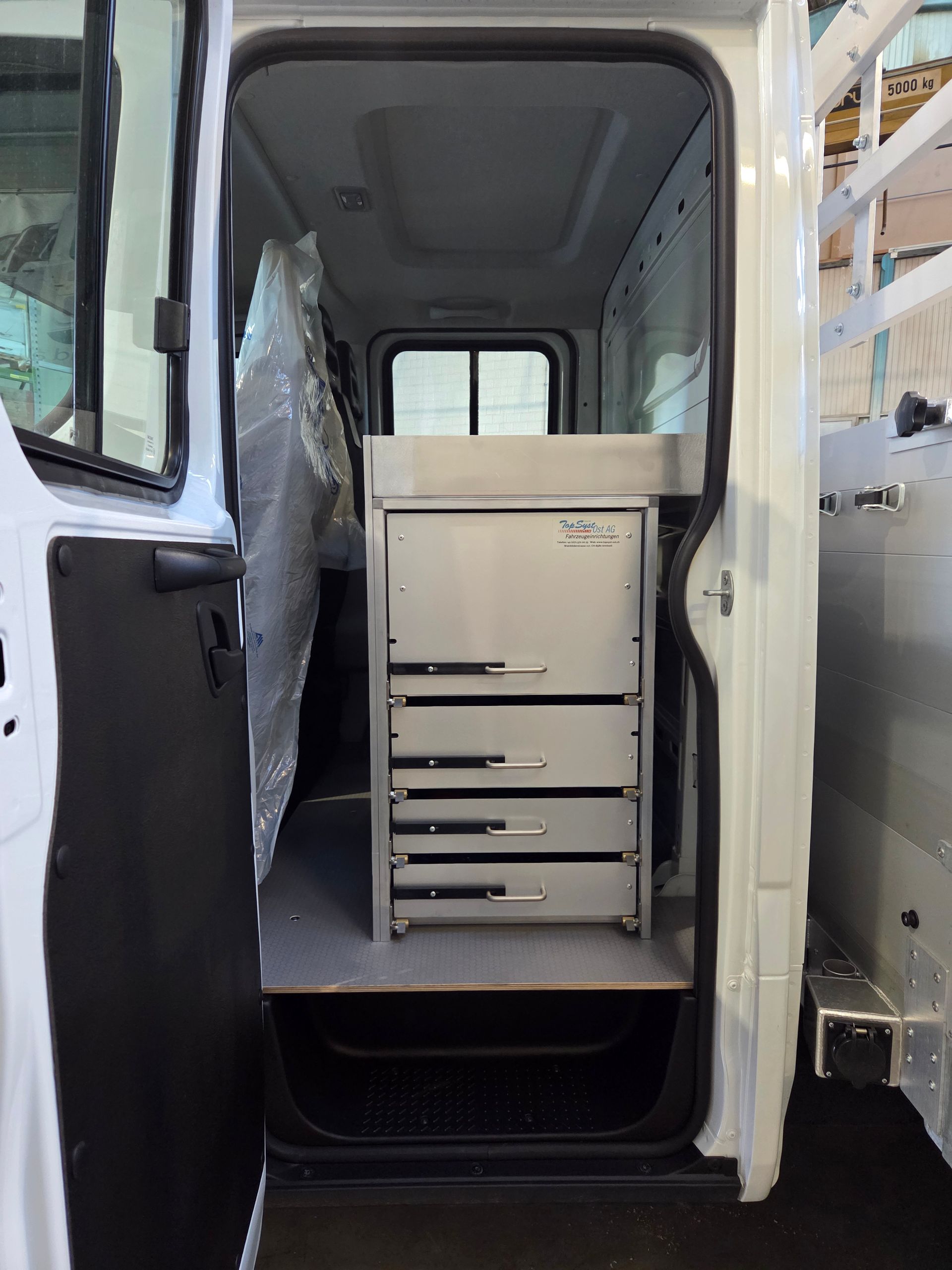 In einem weißen Servicewagen steht im Türrahmen ein Metallschrank mit Schubladen.