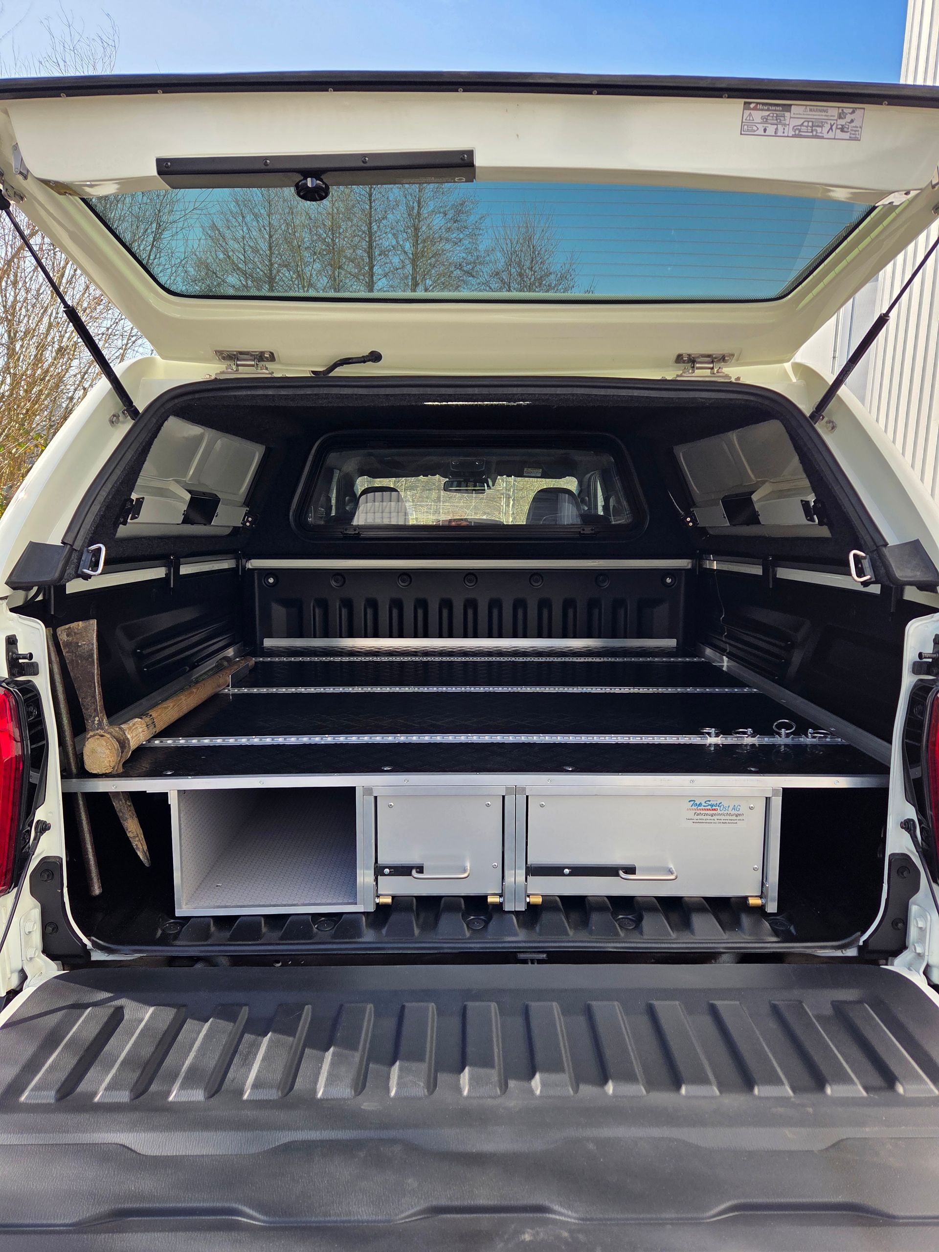 Weiße Pickup-Ladefläche mit schwarzem Baldachin, ausgestattet mit einem Schiebeschubladensystem und Werkzeug.