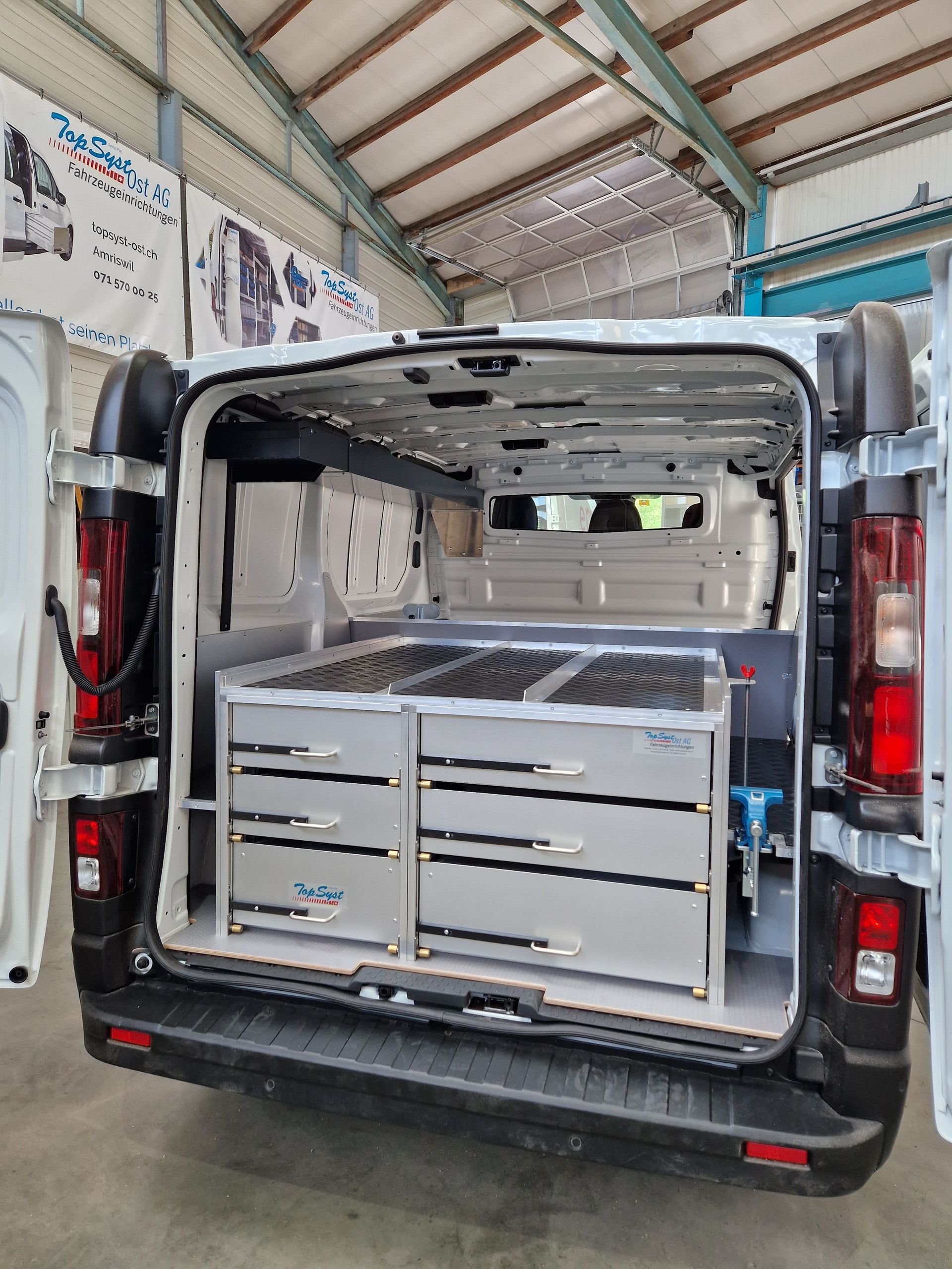 Rückansicht des Innenraums eines weißen Lieferwagens, individuell ausgestattet mit Schubladen und Stauraum für Werkzeuge.