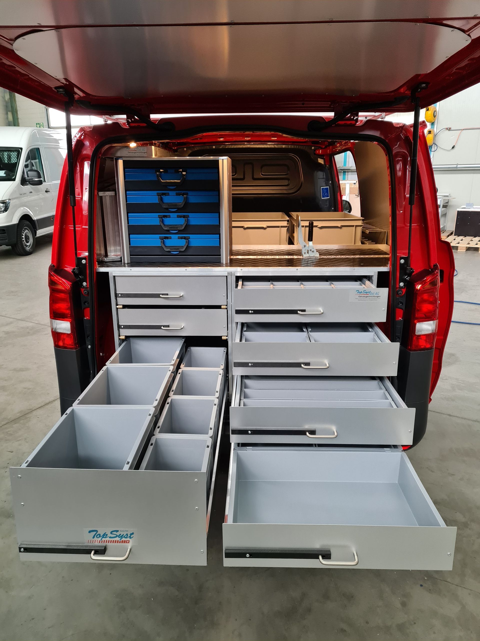 Innenraum eines roten Lieferwagens mit geöffneten Schubladen und Fächern, organisiert für Werkzeuge und Ausrüstung.