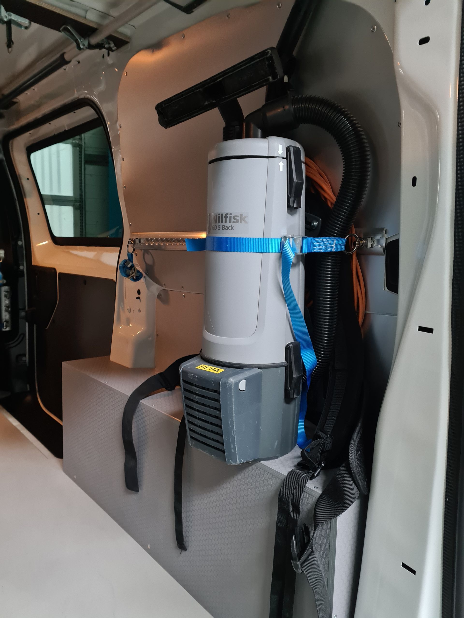 Staubsauger in einem weißen Lieferwagen montiert, mit blauen Gurten und Schläuchen gesichert.