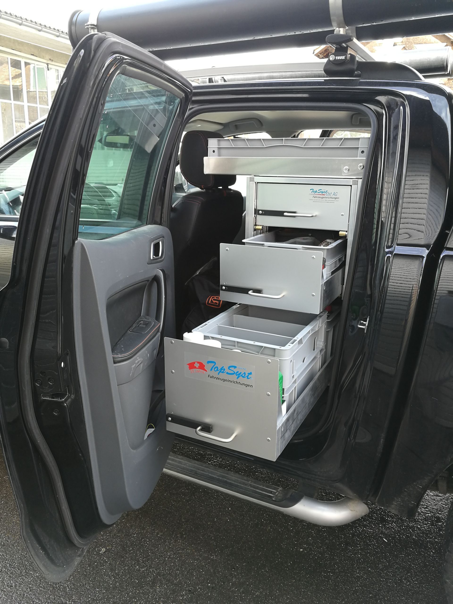 Schwarzer LKW mit geöffneter Tür, hinter der sich mehrere ausziehbare Schubladen zur Aufbewahrung befinden.