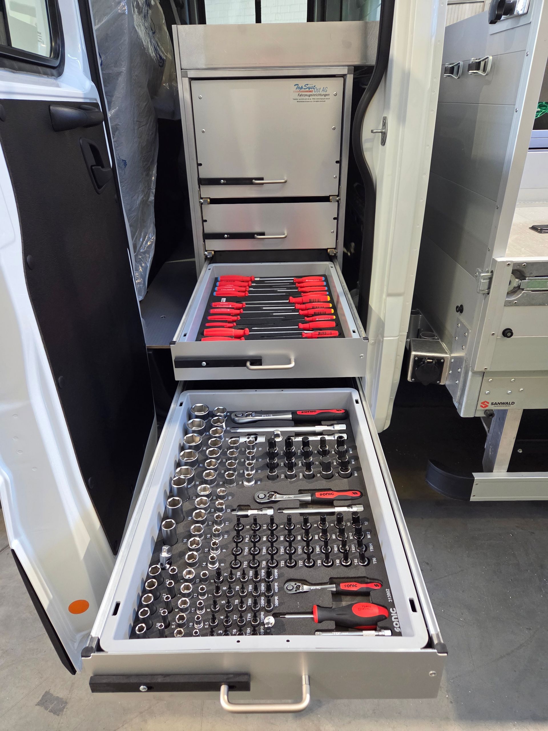 Werkzeugschubladen mit Werkzeugen in einem Lieferwagen. Silberne Schubladen sind geöffnet und enthalten Schraubendreher und Steckschlüssel.