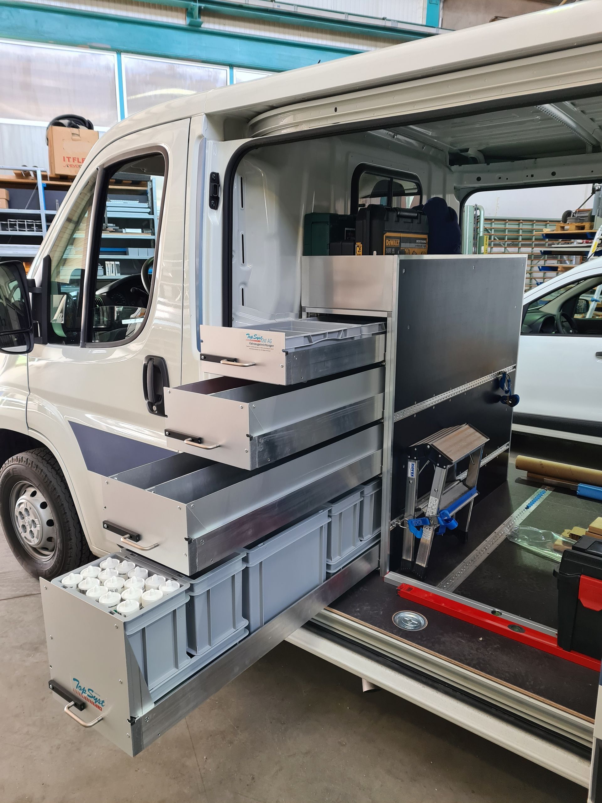 Weißer Lieferwagen mit offener Seite, der Metallschubladen, Werkzeuge und Zubehör in einer Werkstatt enthält.