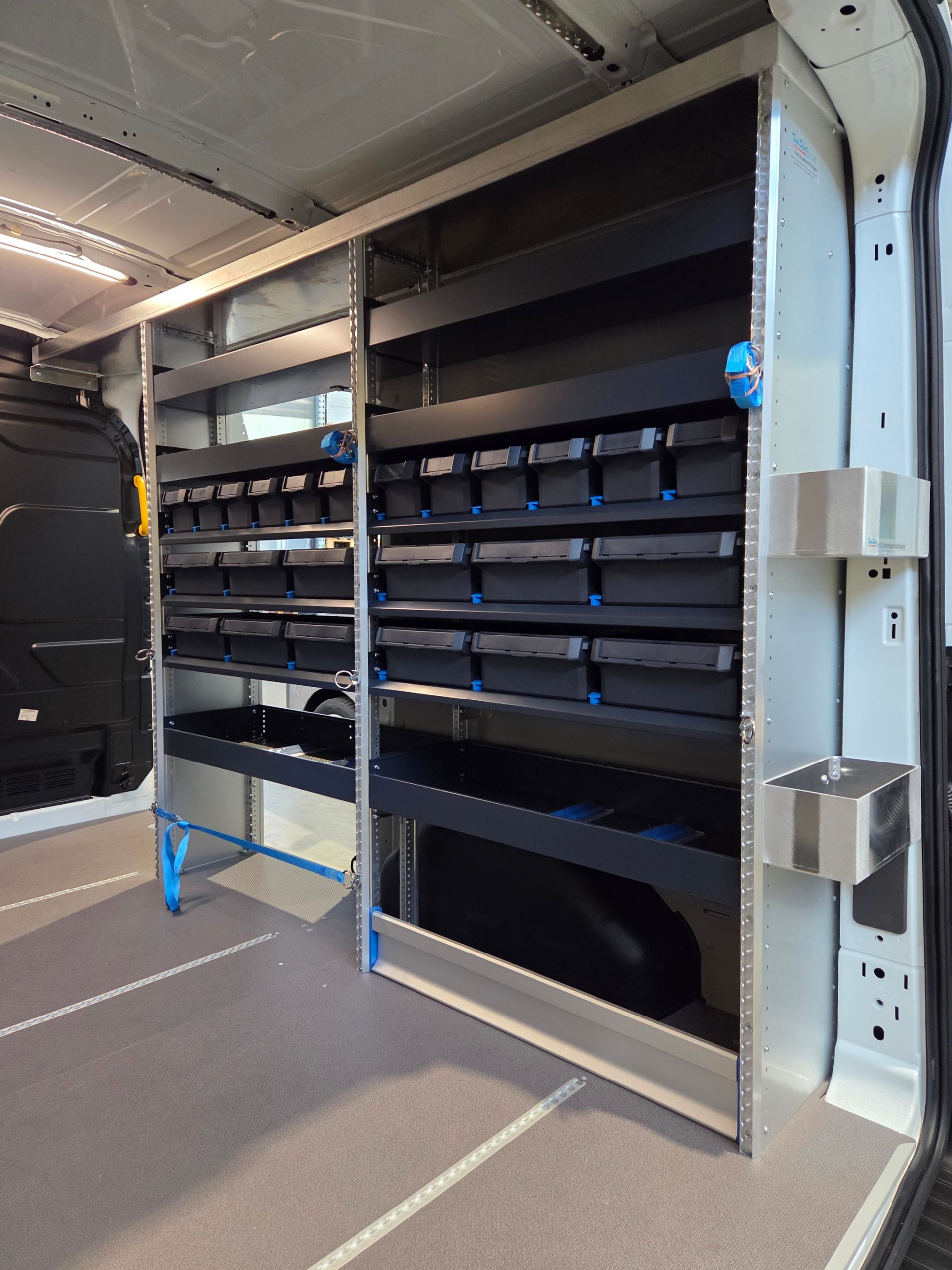 Innenraum eines Lieferwagens mit Regaleinheiten. Schwarze Lagerbehälter, silberne Regale und blaue Stützen.