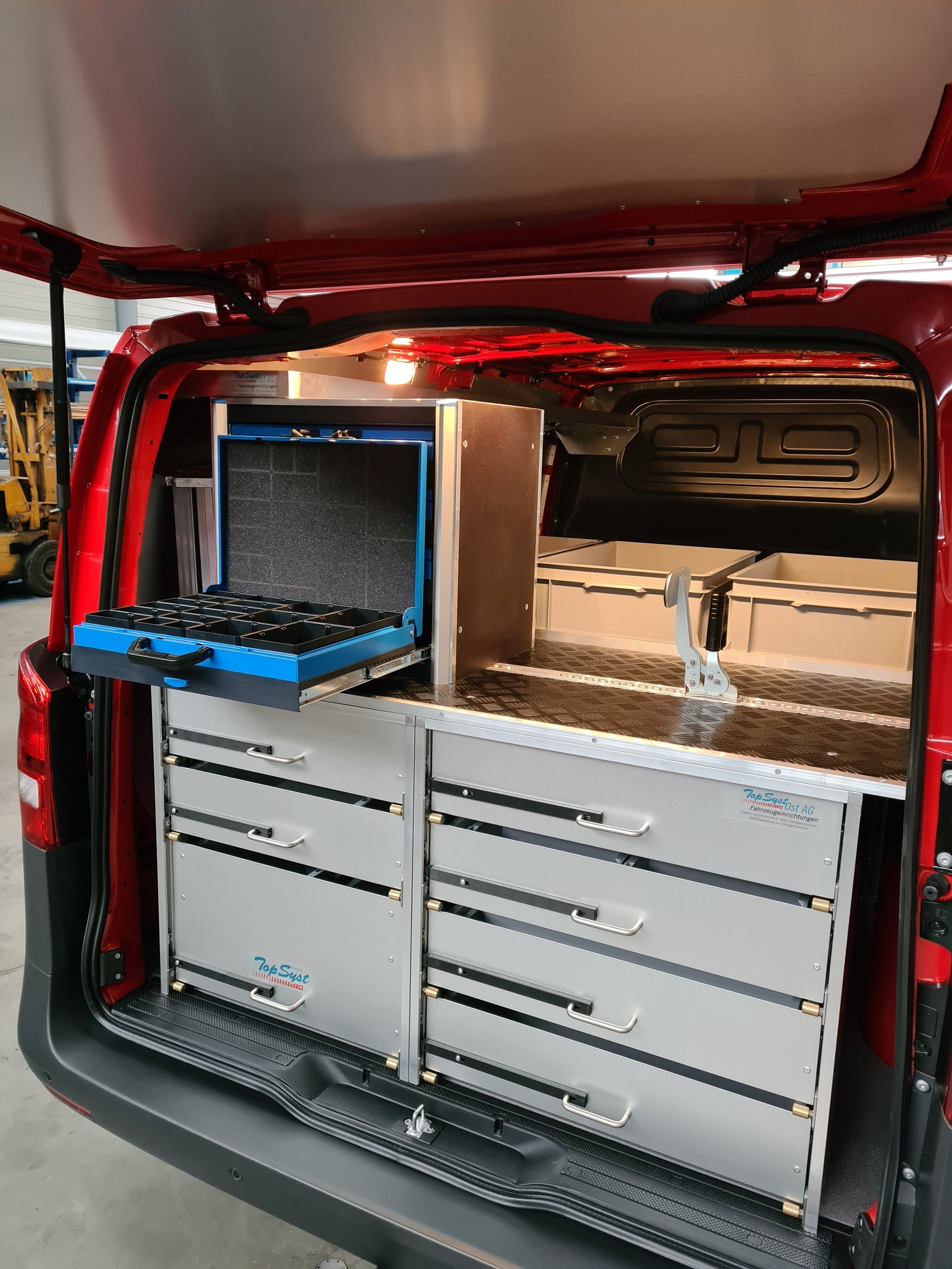 Innenraum eines roten Lieferwagens mit offenen Hintertüren, der einen eingebauten Werkzeugschrank und einen Werkzeugkasten zeigt.