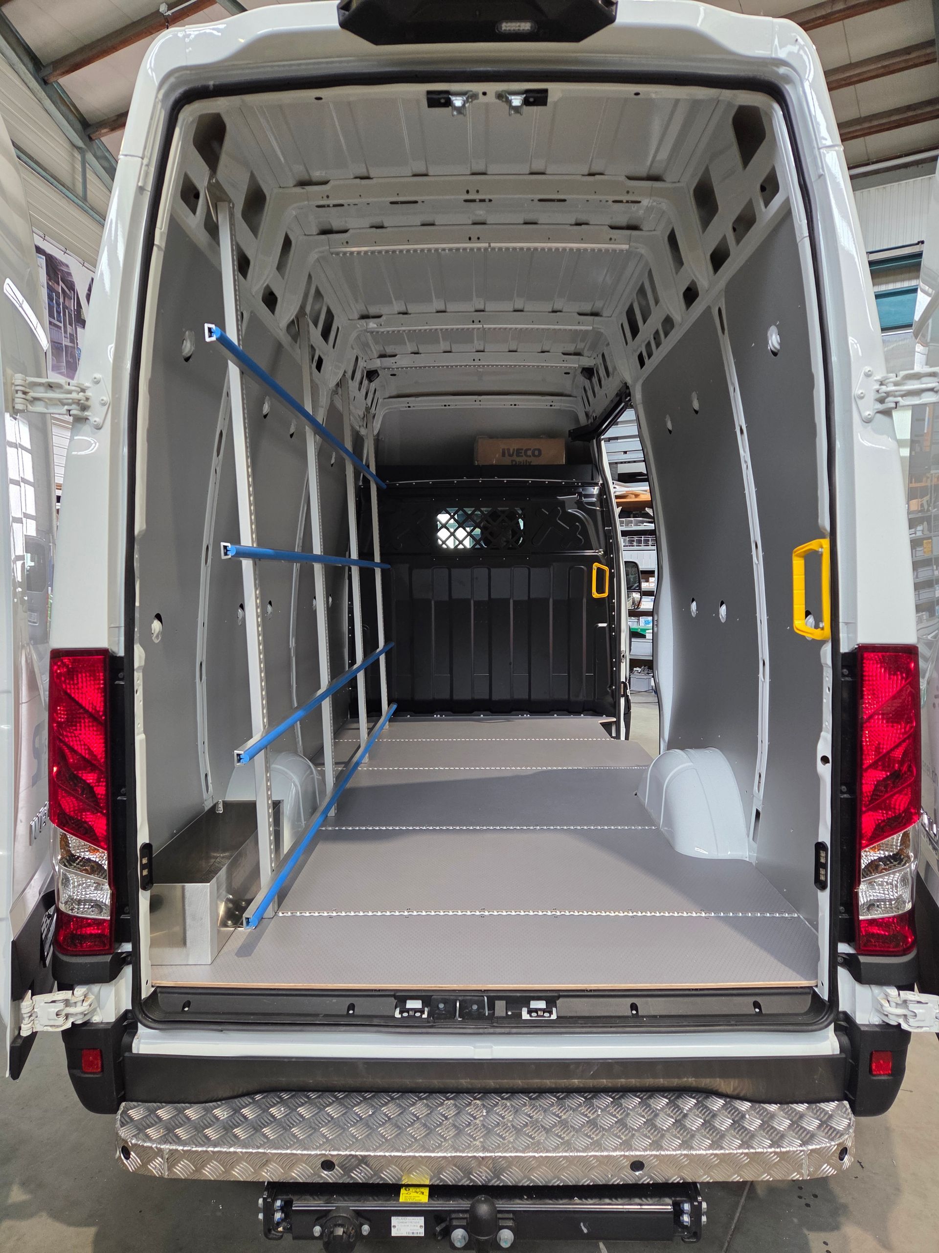 Innenraum eines weißen Lieferwagens mit grauer Verkleidung, Regalen und einer Heckstoßstange aus Diamantblech.