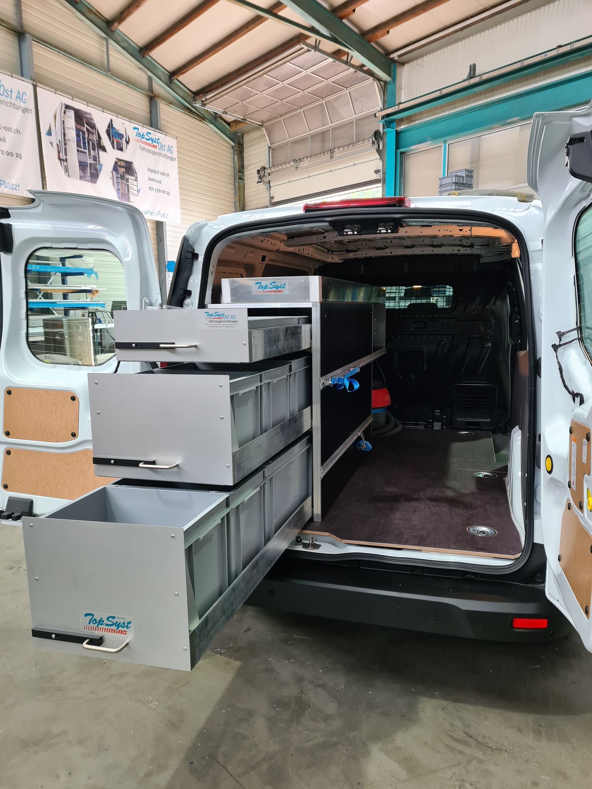 Weißer Lieferwagen mit offener Rückseite, die graue Schubladen freigibt. Innenaufnahme.