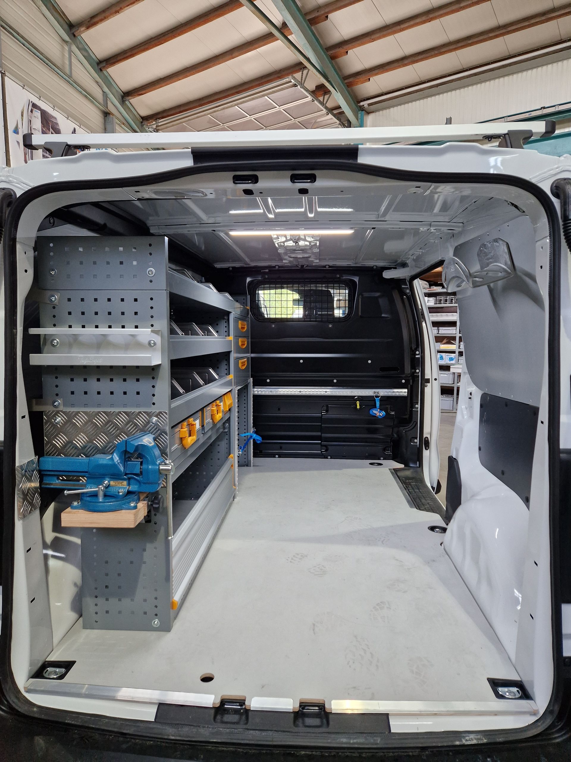 Innenraum eines weißen Lieferwagens mit grauen Regalen und geordneten Werkzeugen; die hinteren Türen sind geöffnet.