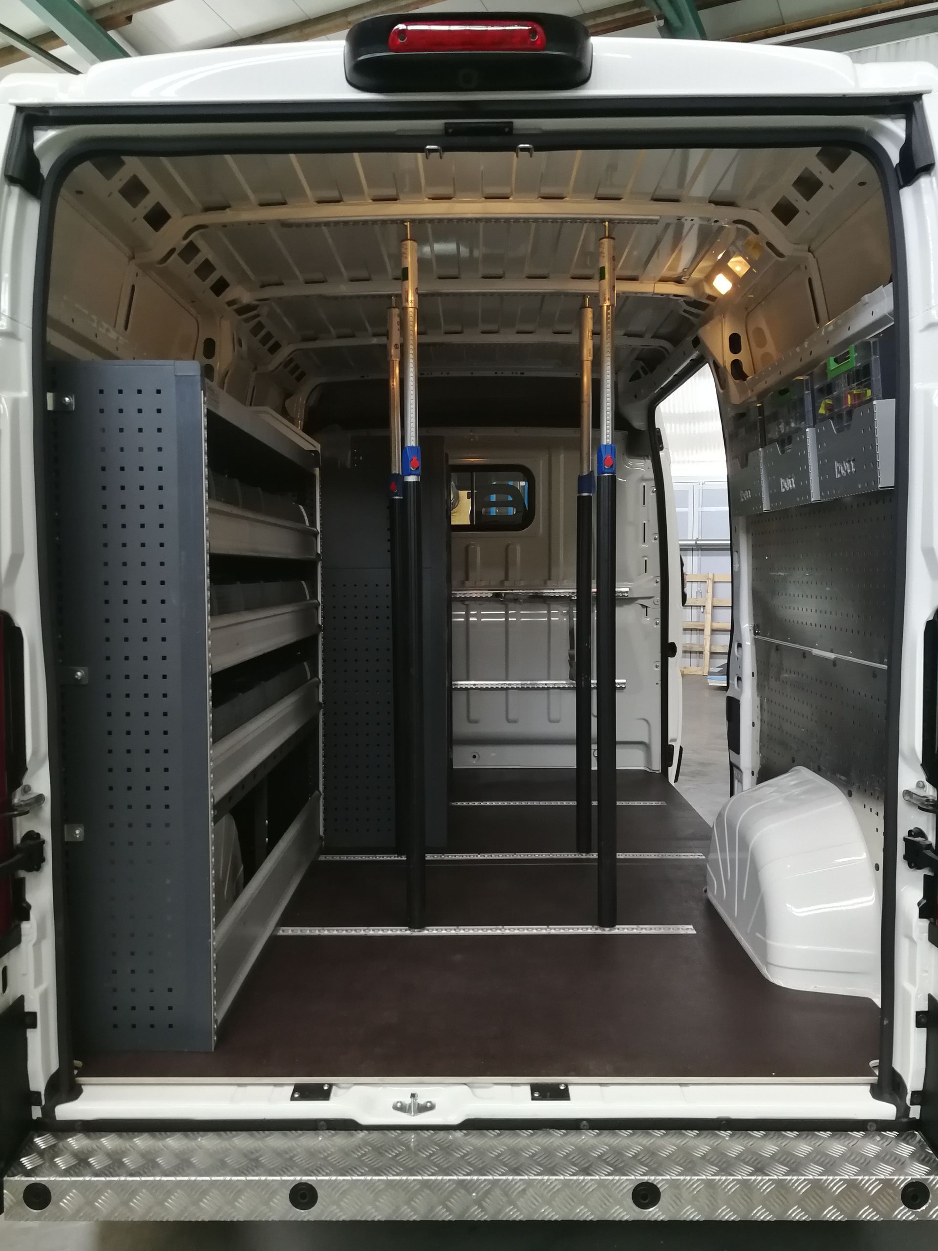Innenansicht eines weißen Lieferwagens mit Regalen auf der linken Seite und Stützbalken, die in der Mitte verlaufen.