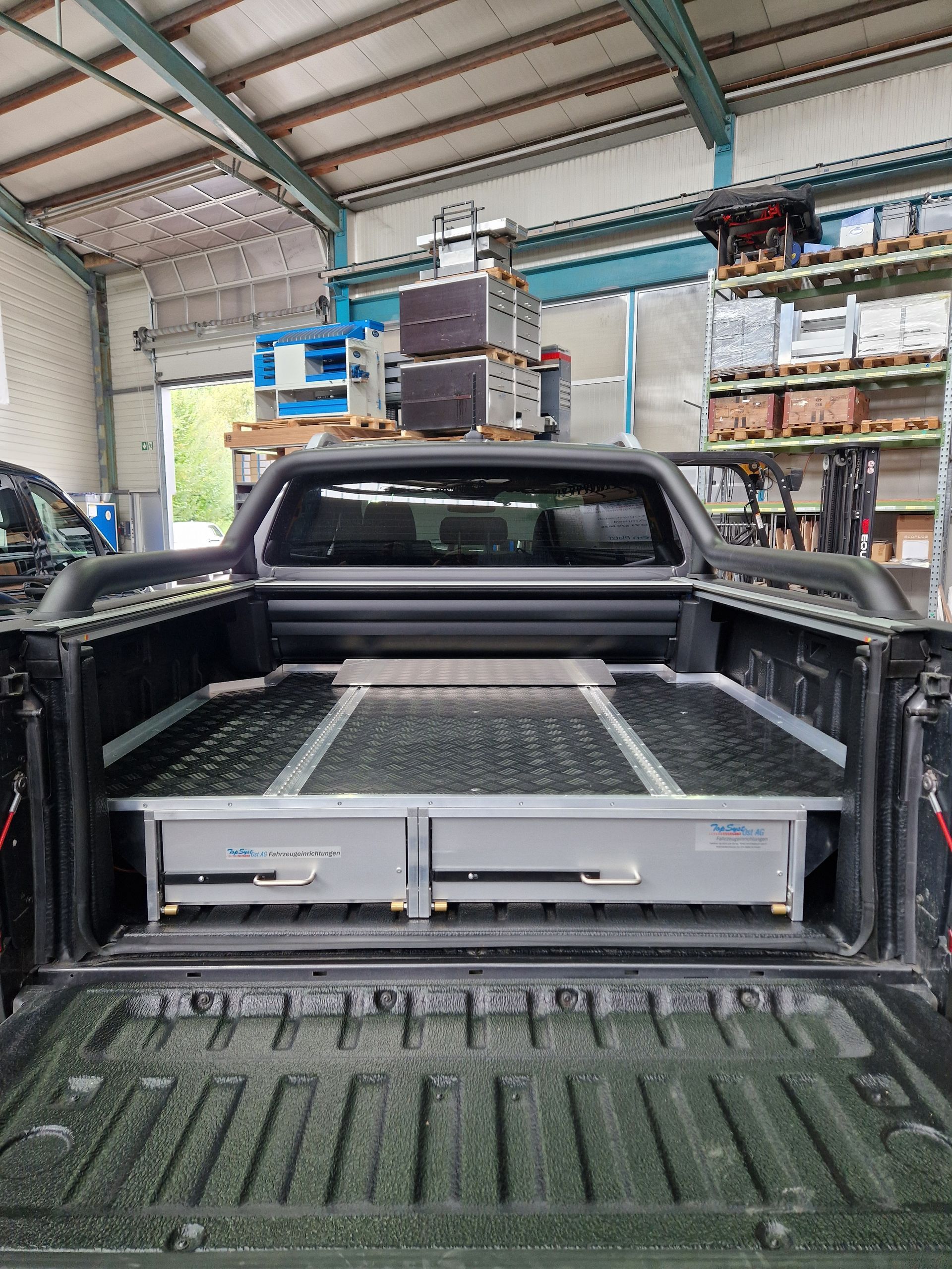 Schwarze Pickup-Ladefläche mit eingebautem Schubladensystem in einer Werkstattumgebung.