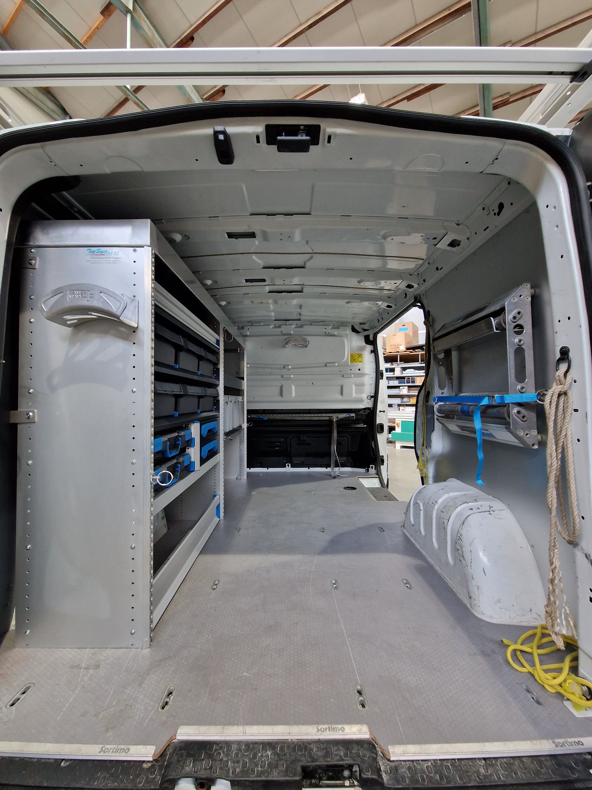 Innenraum eines weißen Lieferwagens mit Metallregalen, leerem Boden und einem Seil.