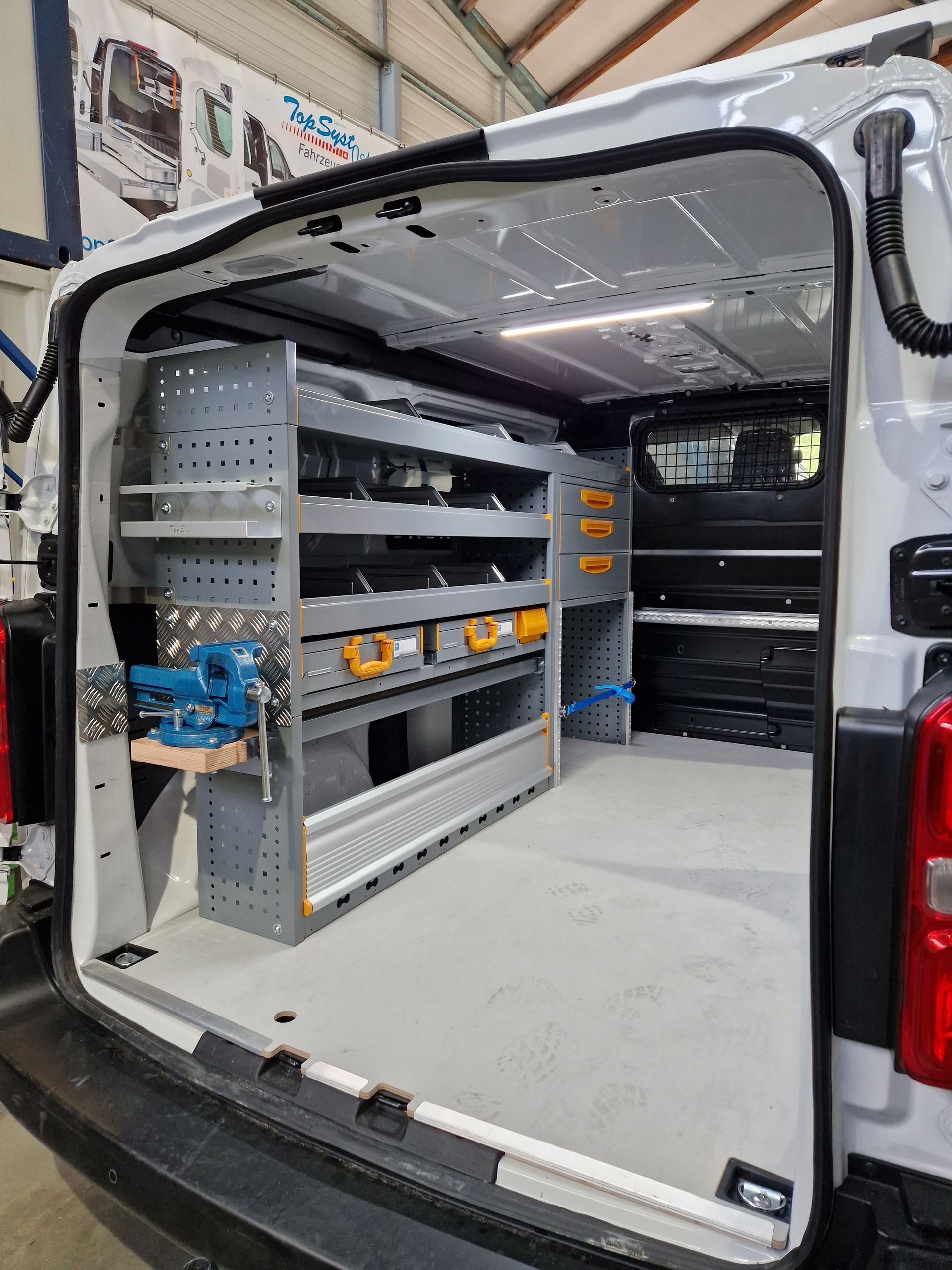 Innenansicht eines weißen Servicewagens mit geordneten Regalen, Schubladen und Werkzeugen.