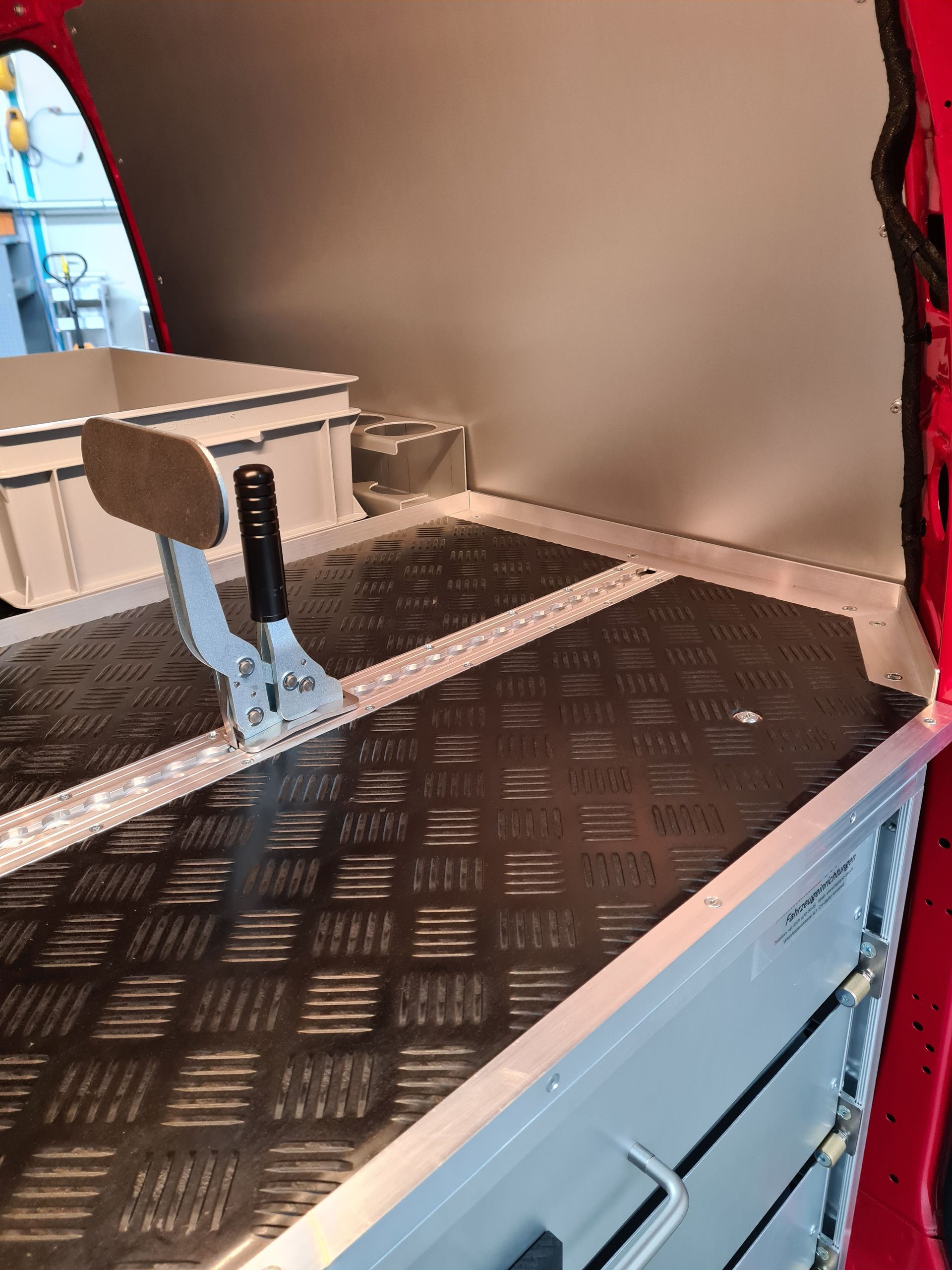 Innenraum eines roten Fahrzeugs mit Diamantplattenboden, Aluminiumschränken und einem schwarzen Hebel.