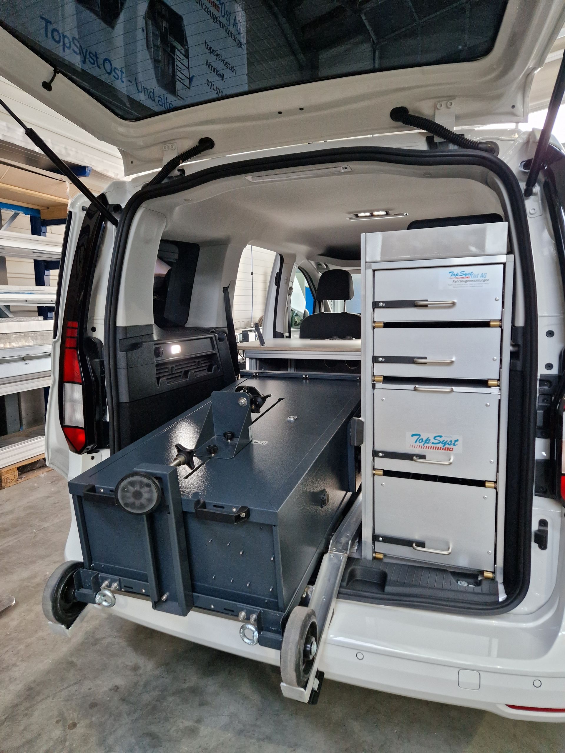 Offener weißer Van-Innenraum mit ausziehbarer Rollstuhlrampe und Aufbewahrungsschubladen.