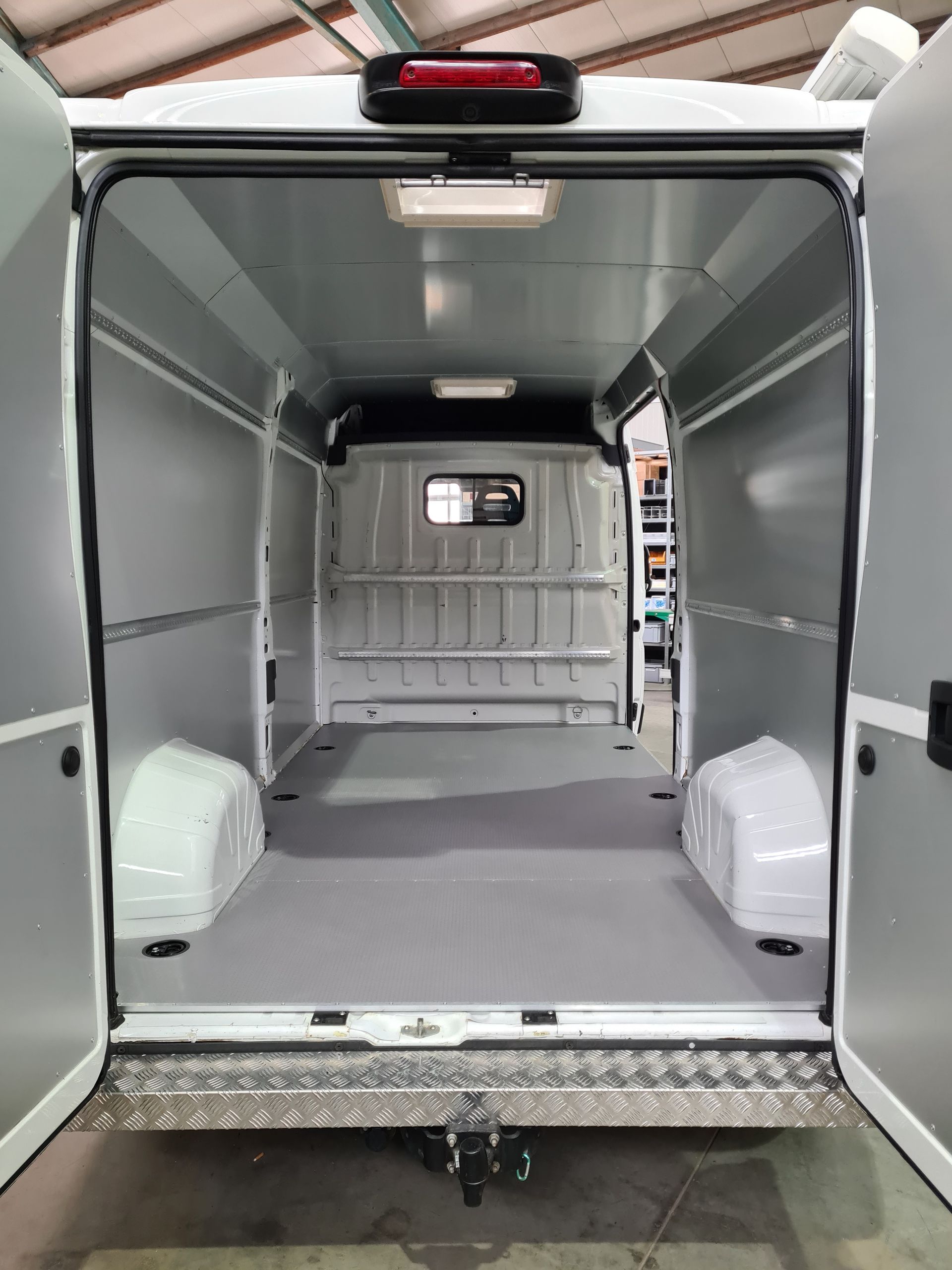 Leerer weißer Lieferwageninnenraum mit grauen Wänden und Boden. Hintertüren offen.