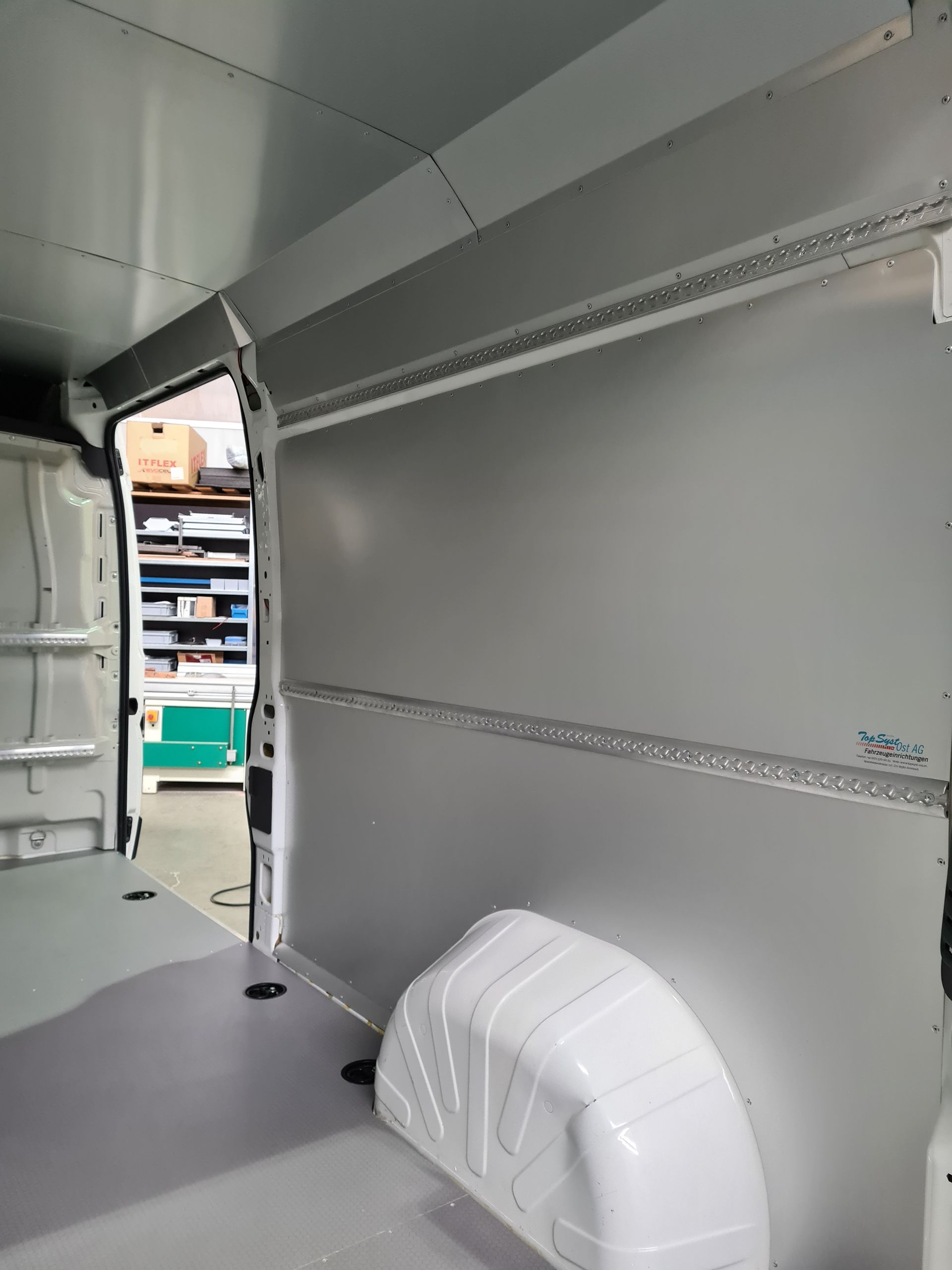 Innenansicht eines weißen Lieferwagens mit grauen Wänden, Schienen zur Ladungsbeförderung und einem Radkasten.