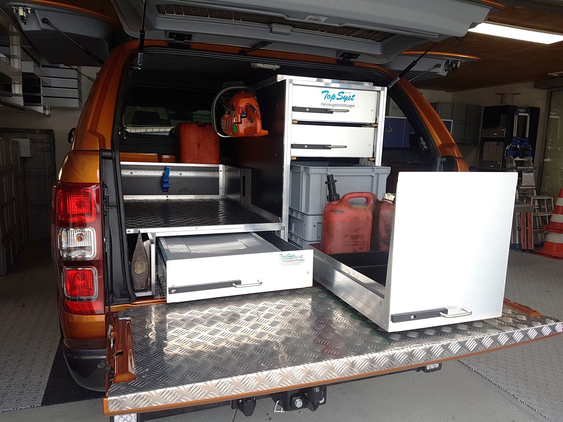 Orangefarbene Ladefläche eines Pickups mit offenen Schubladen und Werkzeugen; die Kulisse scheint eine Garage oder Werkstatt zu sein.