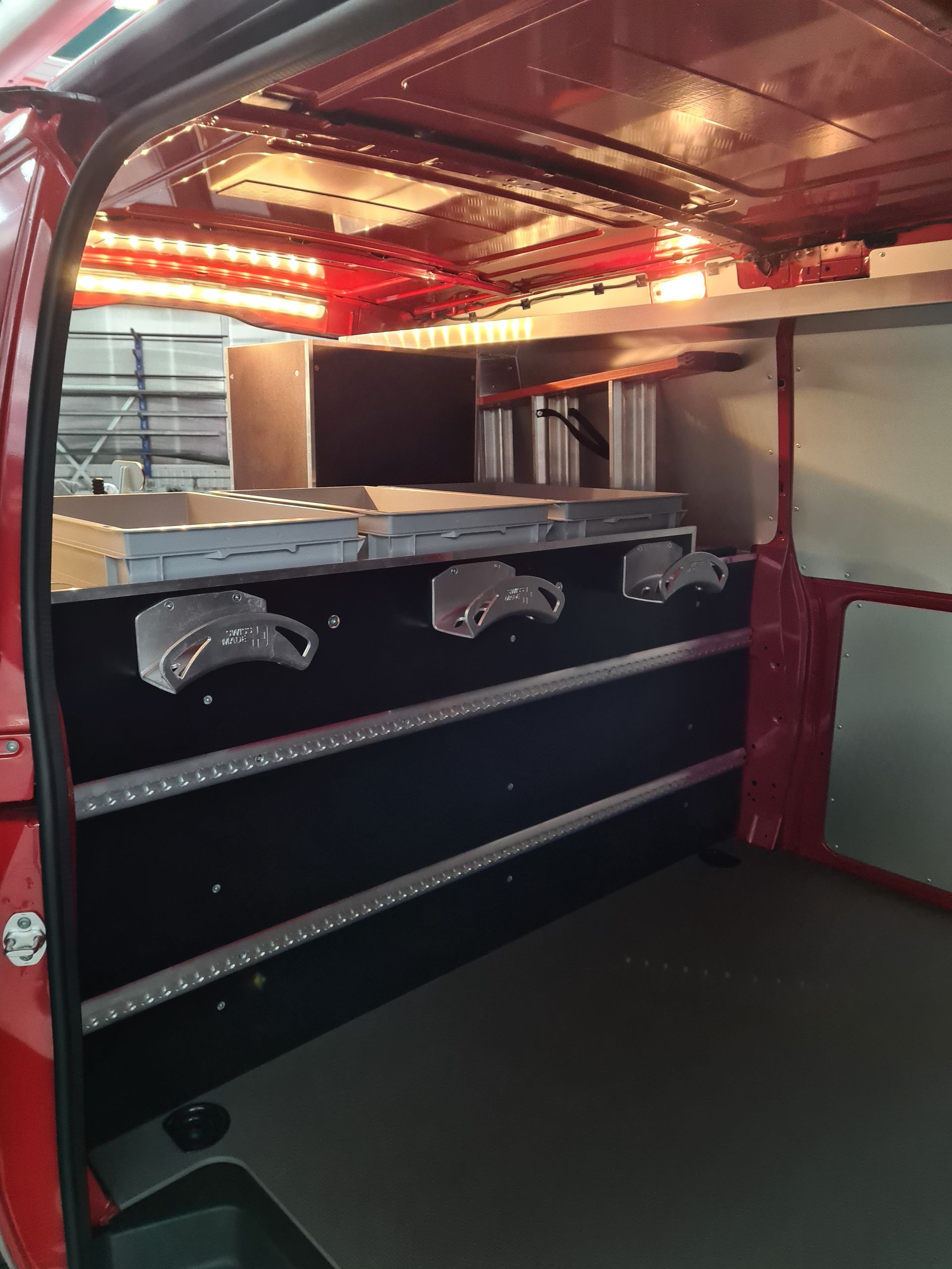 Innenraum eines roten Fahrzeugs mit Decken- und Streifenbeleuchtung. Silberne Armaturen an einer schwarzen Wand.