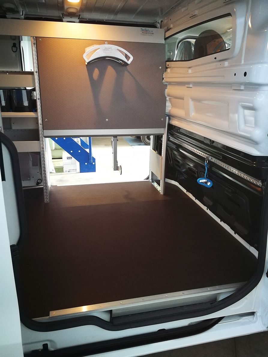 Innenraum eines weißen Lieferwagens mit dunkelbraunem Boden, Regalen und einem hängenden Gesichtsschutz.