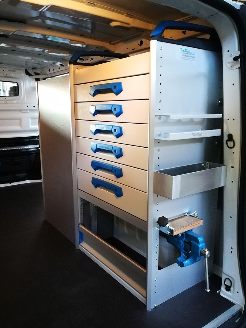 Innenansicht eines Arbeitswagens mit Metallschränken, Schubladen, Regalen und einem blauen Schraubstock.