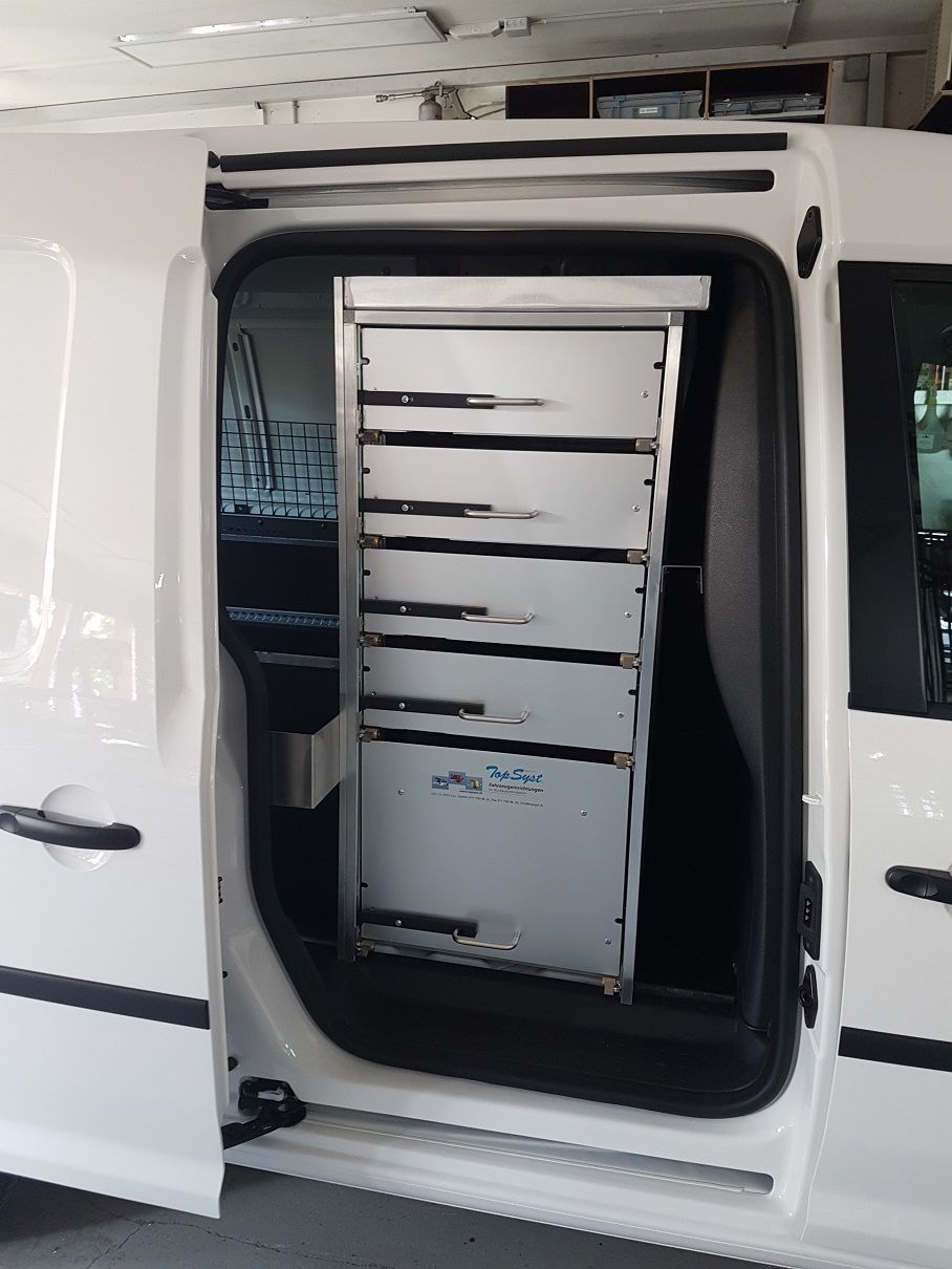 Hinter der offenen Tür eines weißen Lieferwagens steht ein hoher, silberner Lagerschrank mit mehreren Schubladen.