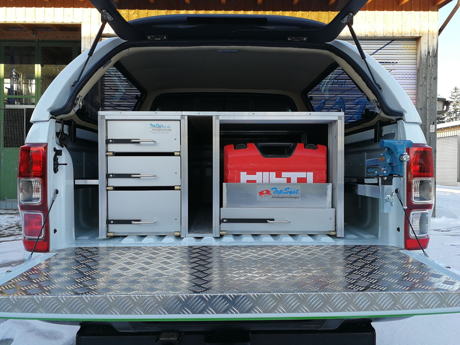 Weiße Pickup-Ladefläche mit organisierter Werkzeugaufbewahrung; Hilti-Werkzeugkasten, Schubladen und montierter Schraubstock.