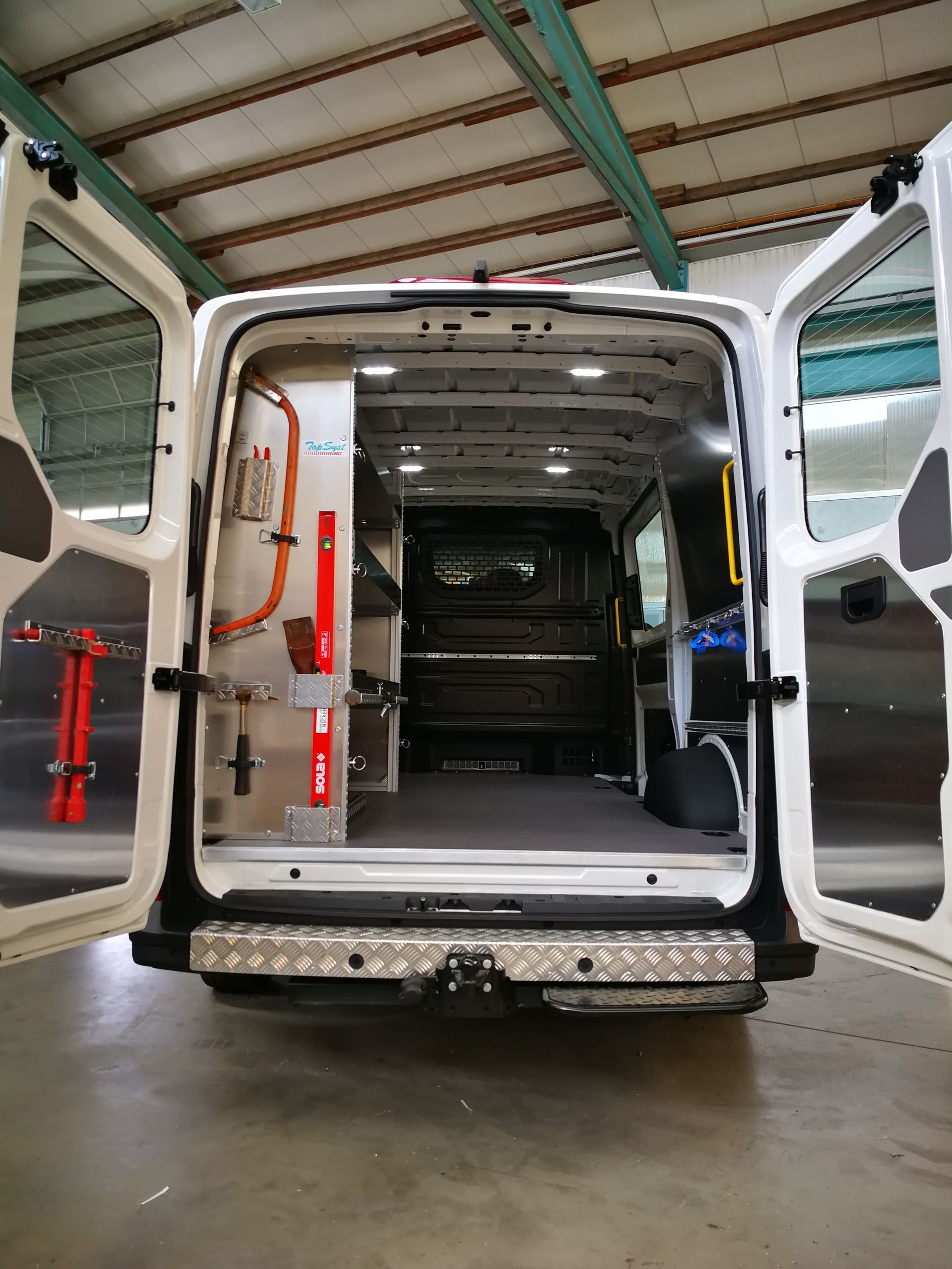 Offene Ladefläche eines weißen Servicewagens mit Regalen und Werkzeug darin.