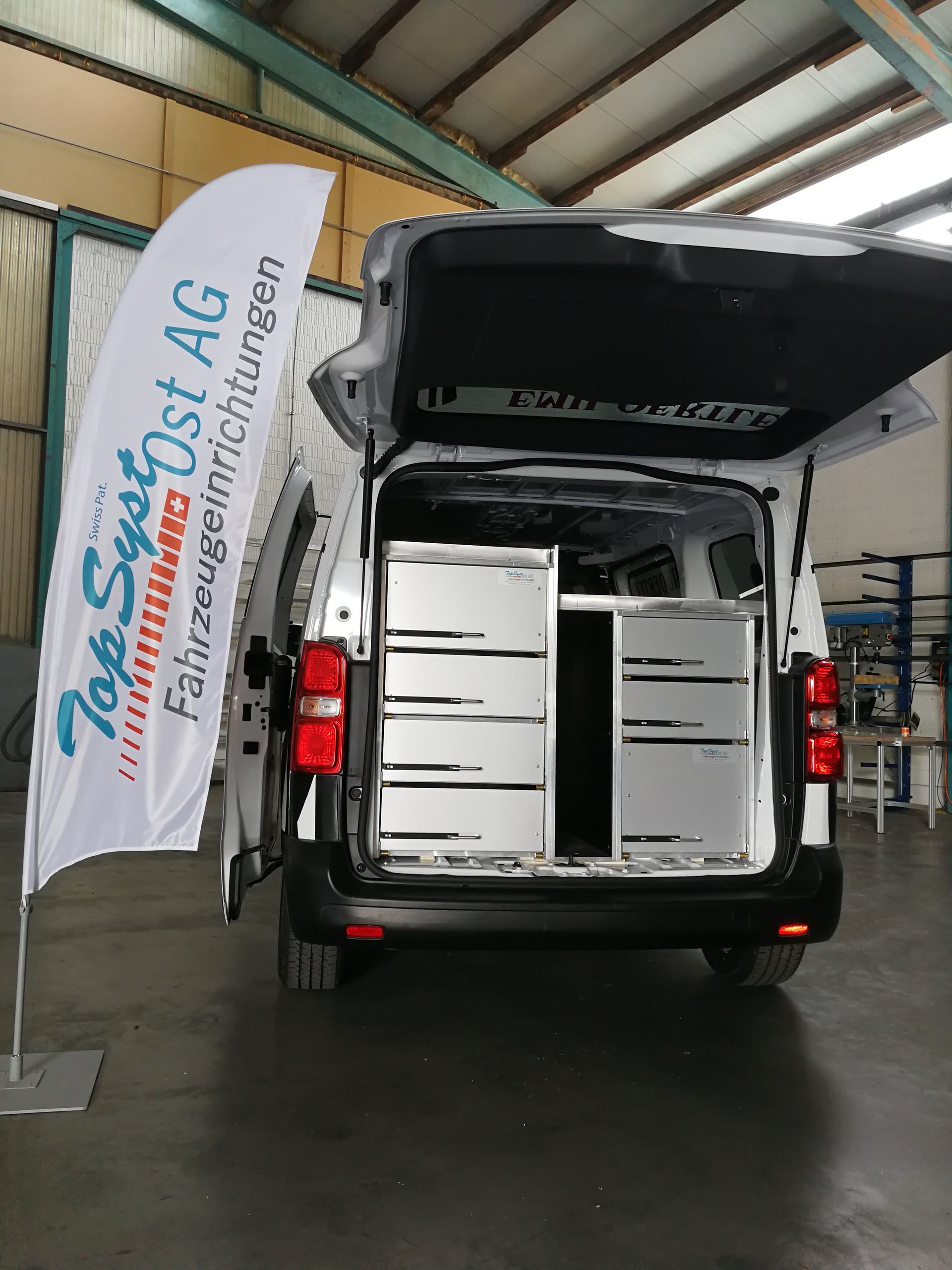 Ein Lieferwagen mit offenem Kofferraum und einer Fahne mit der Aufschrift „Top Systems AG“