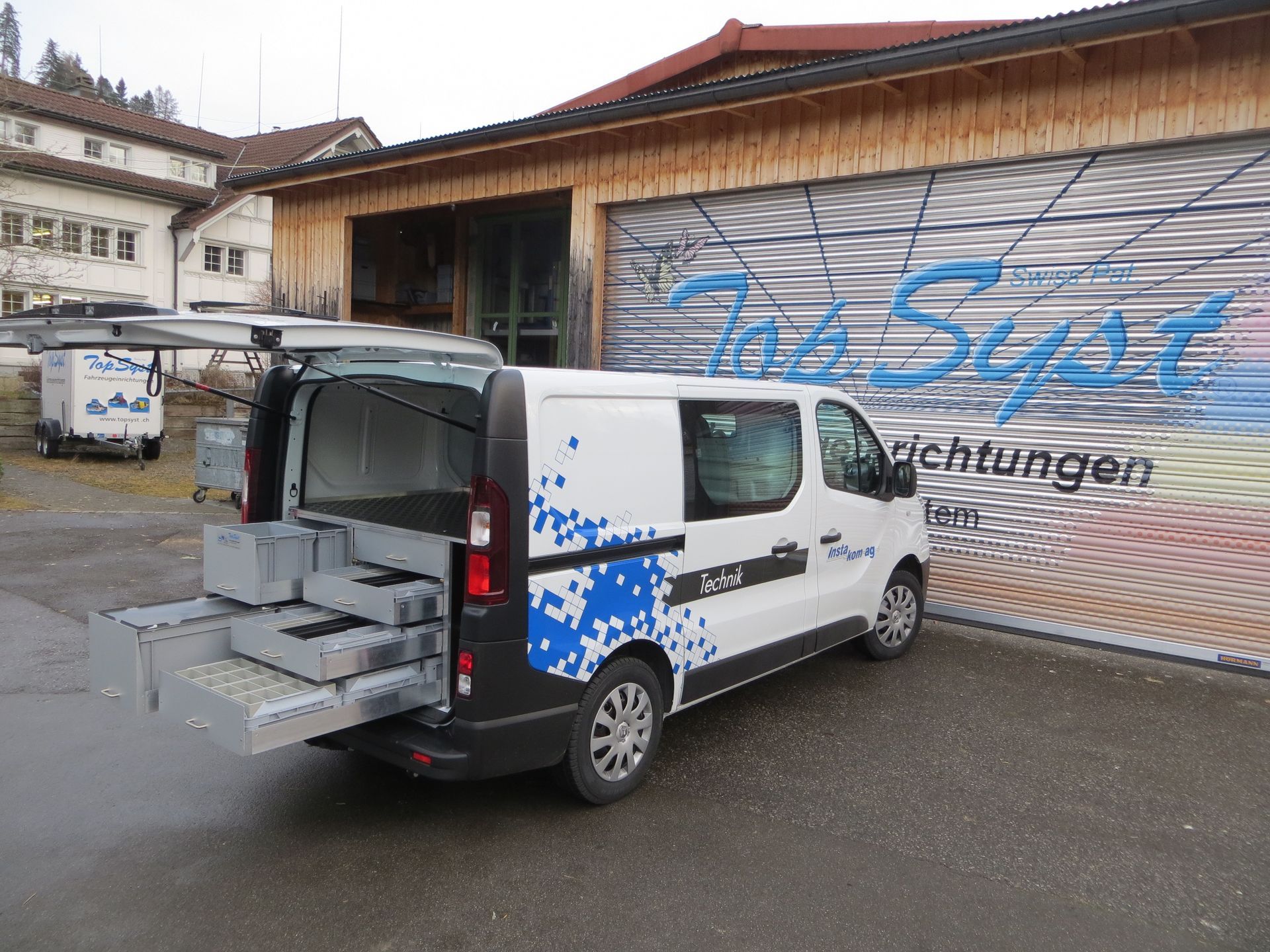 Ein weißer Lieferwagen mit offenem Kofferraum steht vor einem Gebäude.