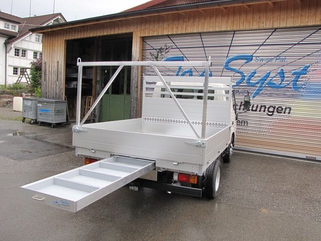 Ein LKW mit einer Ladefläche auf der Ladefläche steht vor einer Garage.