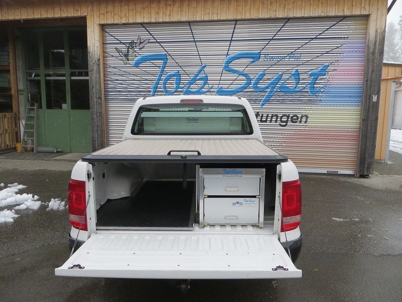 Ein weißer Lastwagen mit offener Hintertür steht vor einem Garagentor.