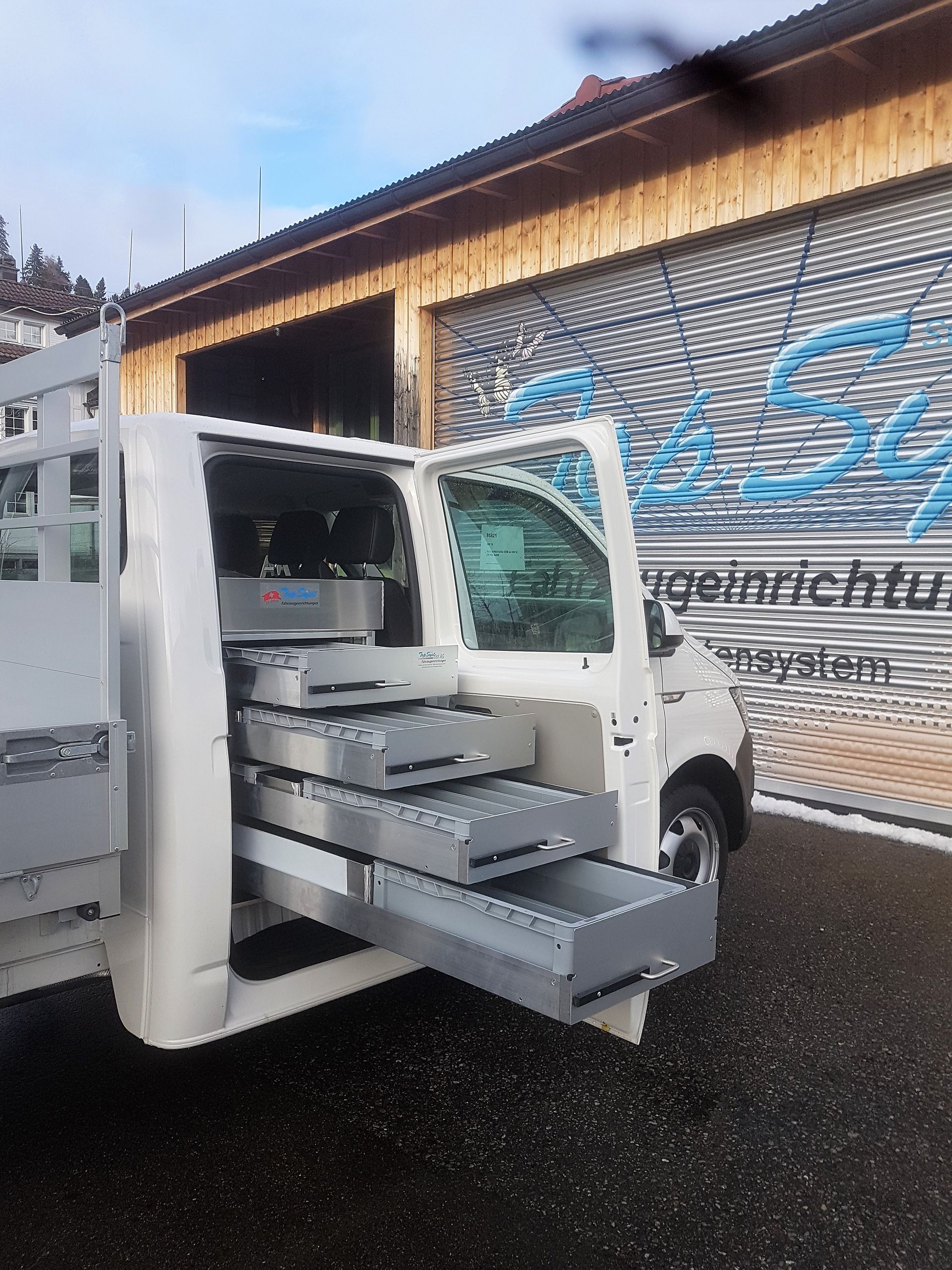 Ein weißer Lastwagen mit geöffneten Schubladen steht vor einem Gebäude.