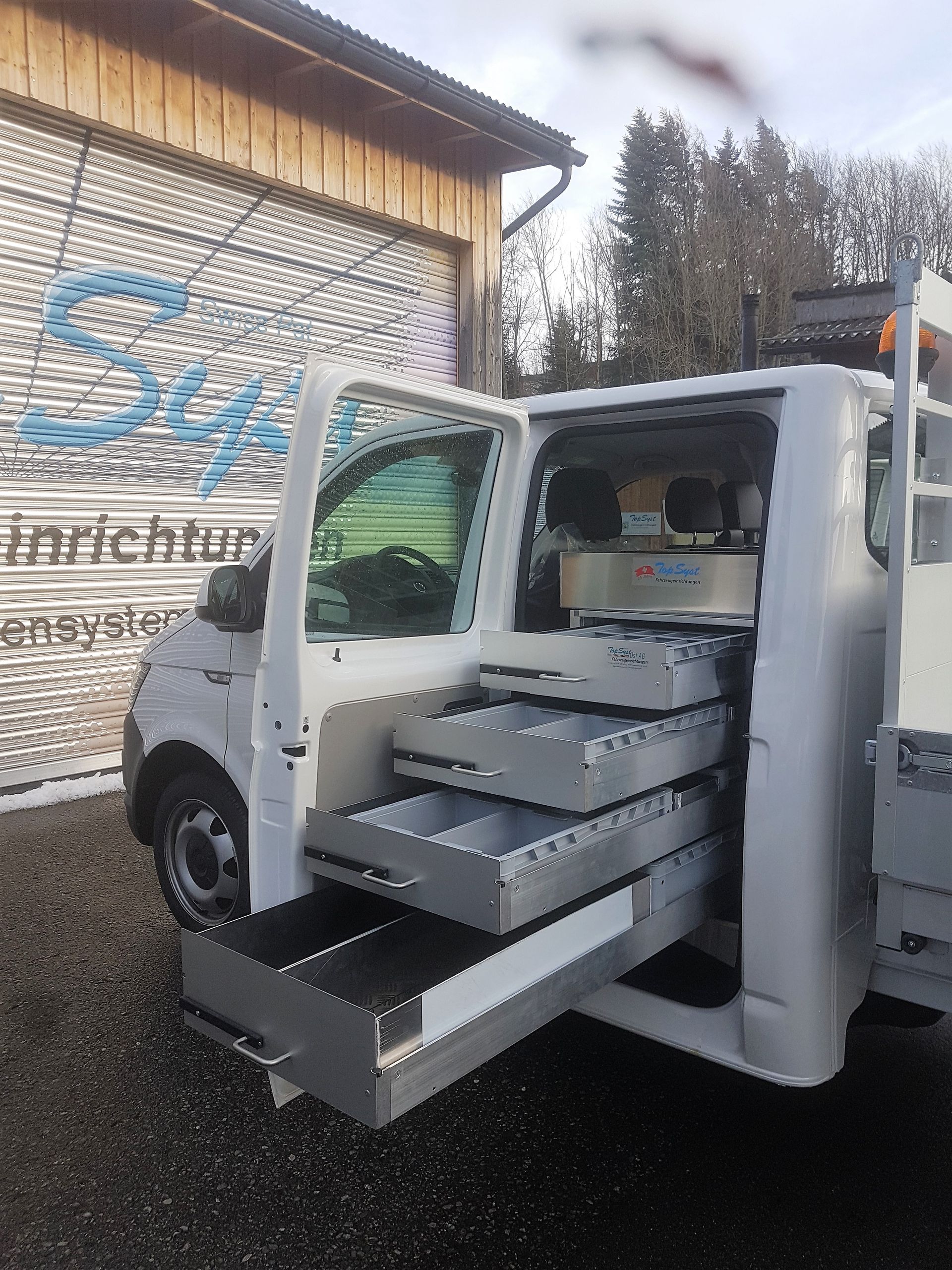 Ein weißer Lieferwagen mit Schubladen auf der Ladefläche steht vor einem Gebäude.