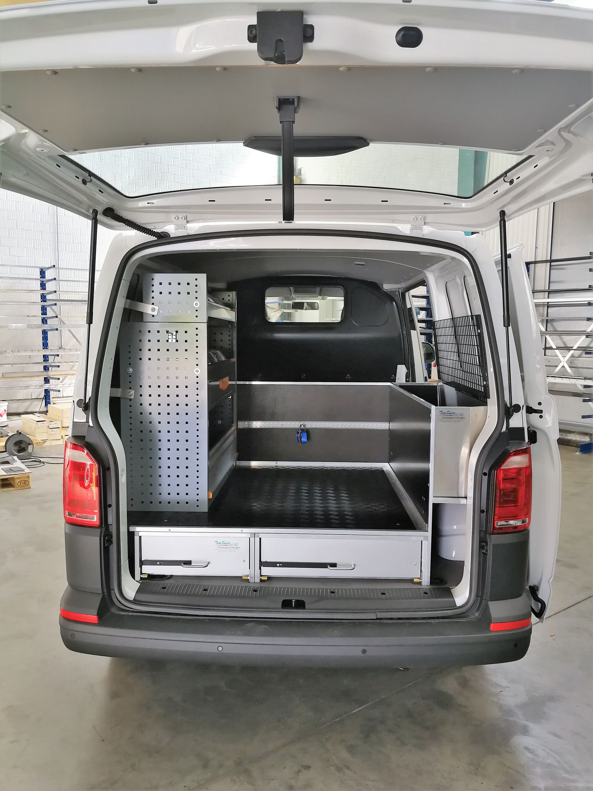 Die Ladefläche eines weißen Lieferwagens mit offenem Kofferraum in einer Lagerhalle.