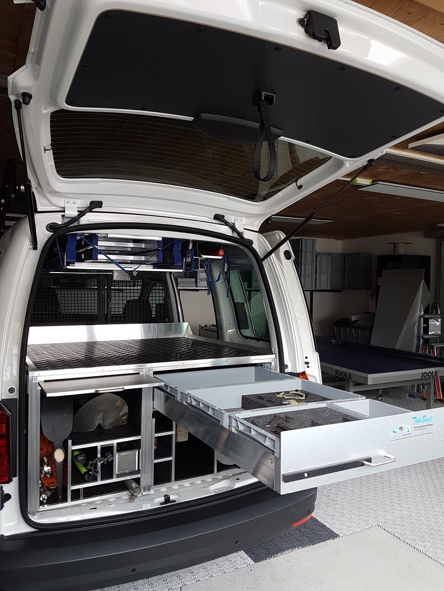 Ein weißer Lieferwagen mit offenem Kofferraum steht in einer Garage.