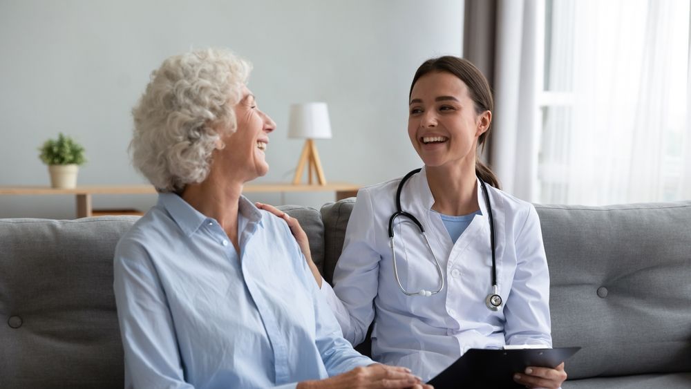 A doctor is talking to an elderly woman while sitting on a couch.