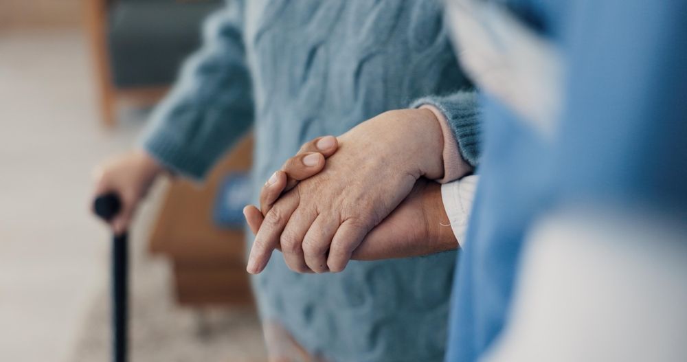 A woman is holding the hand of an elderly woman with a cane.