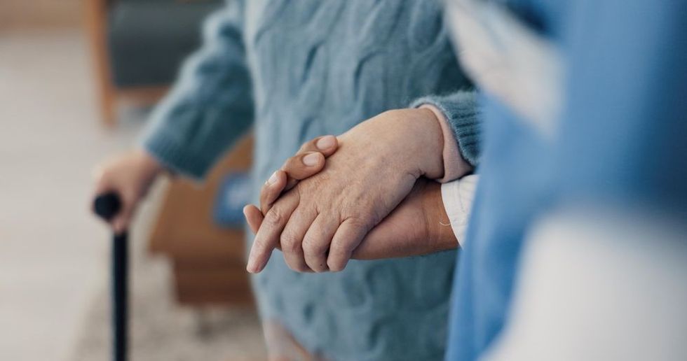 A woman is holding the hand of an elderly woman with a cane.