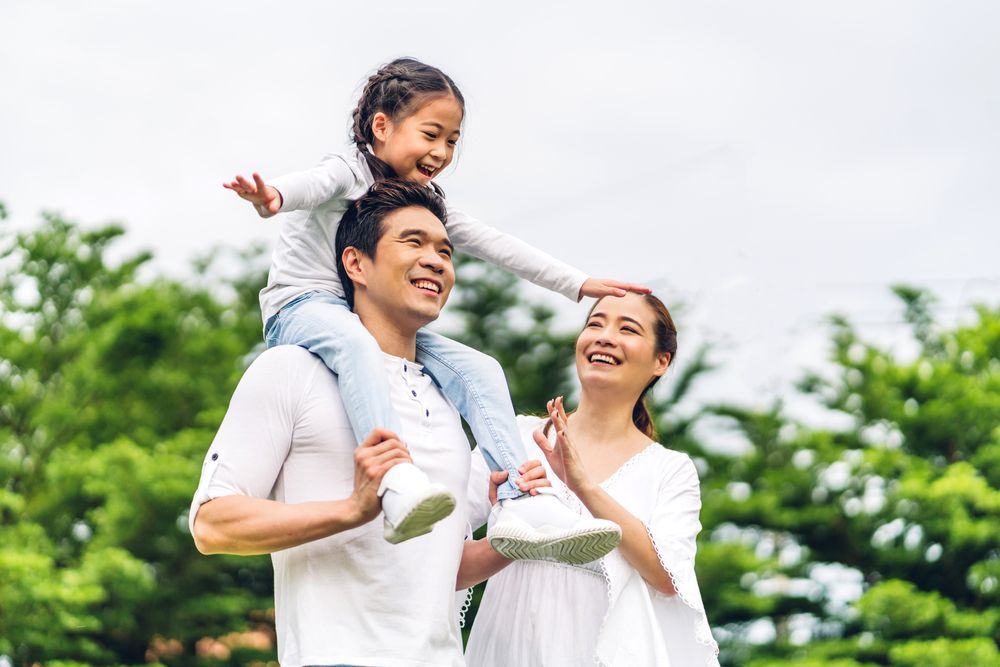A man is carrying a little girl on his shoulders in a park.