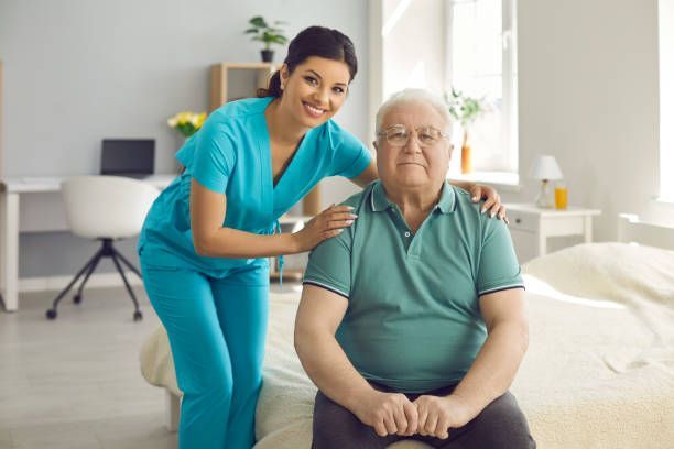 An elderly woman is sitting on a bed with her hands on her chest.