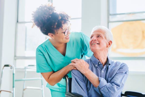 A nurse is helping an elderly man walk with a cane in a living room.