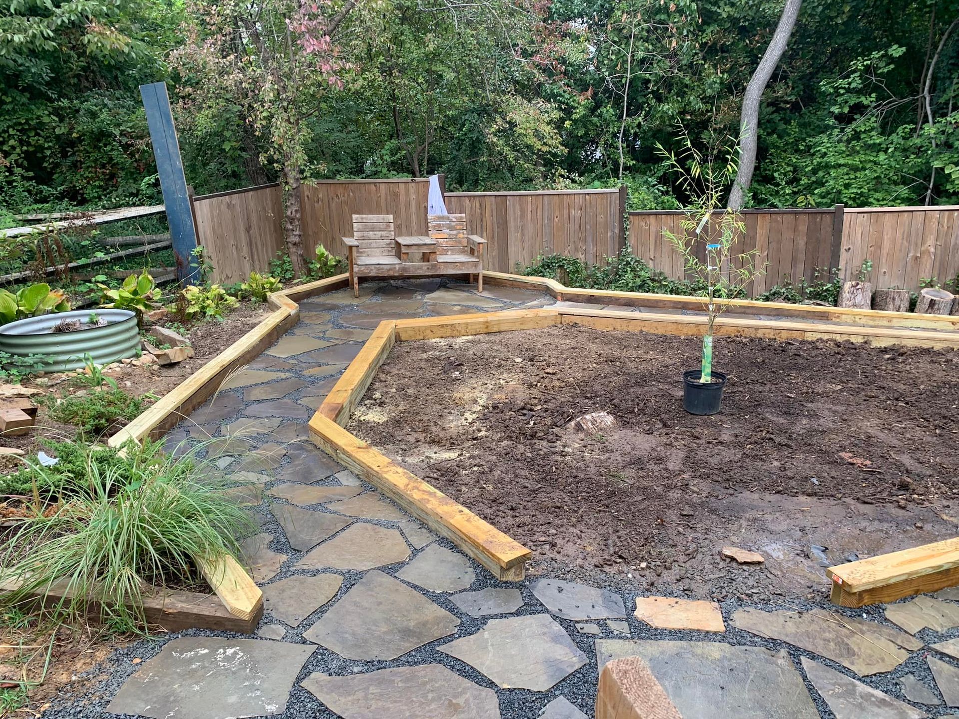A backyard garden with a stone path, raised beds, wooden benches, and a wooden fence.