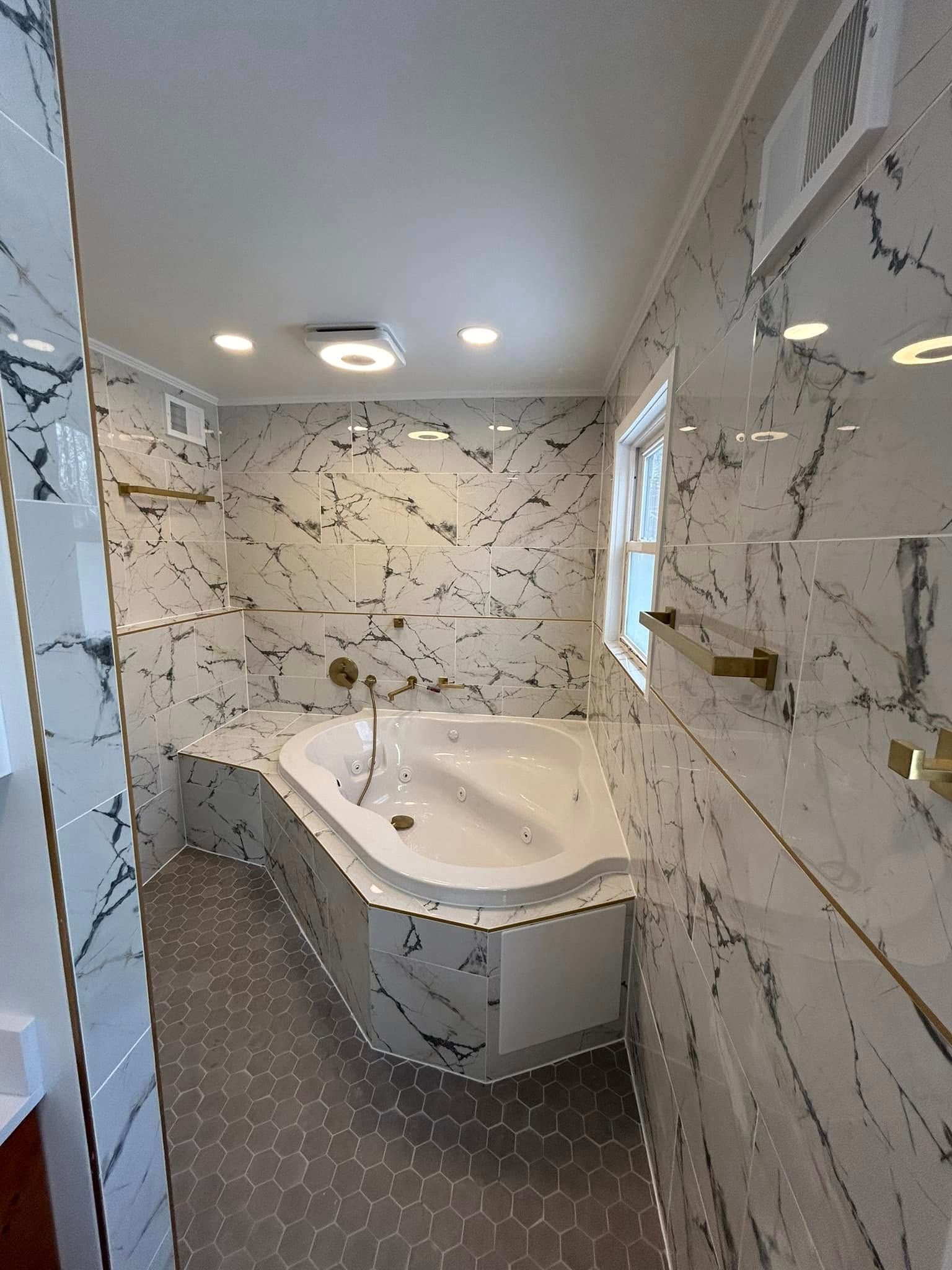 Bathroom with marble walls, a white tub, gray tile floor, and gold fixtures.