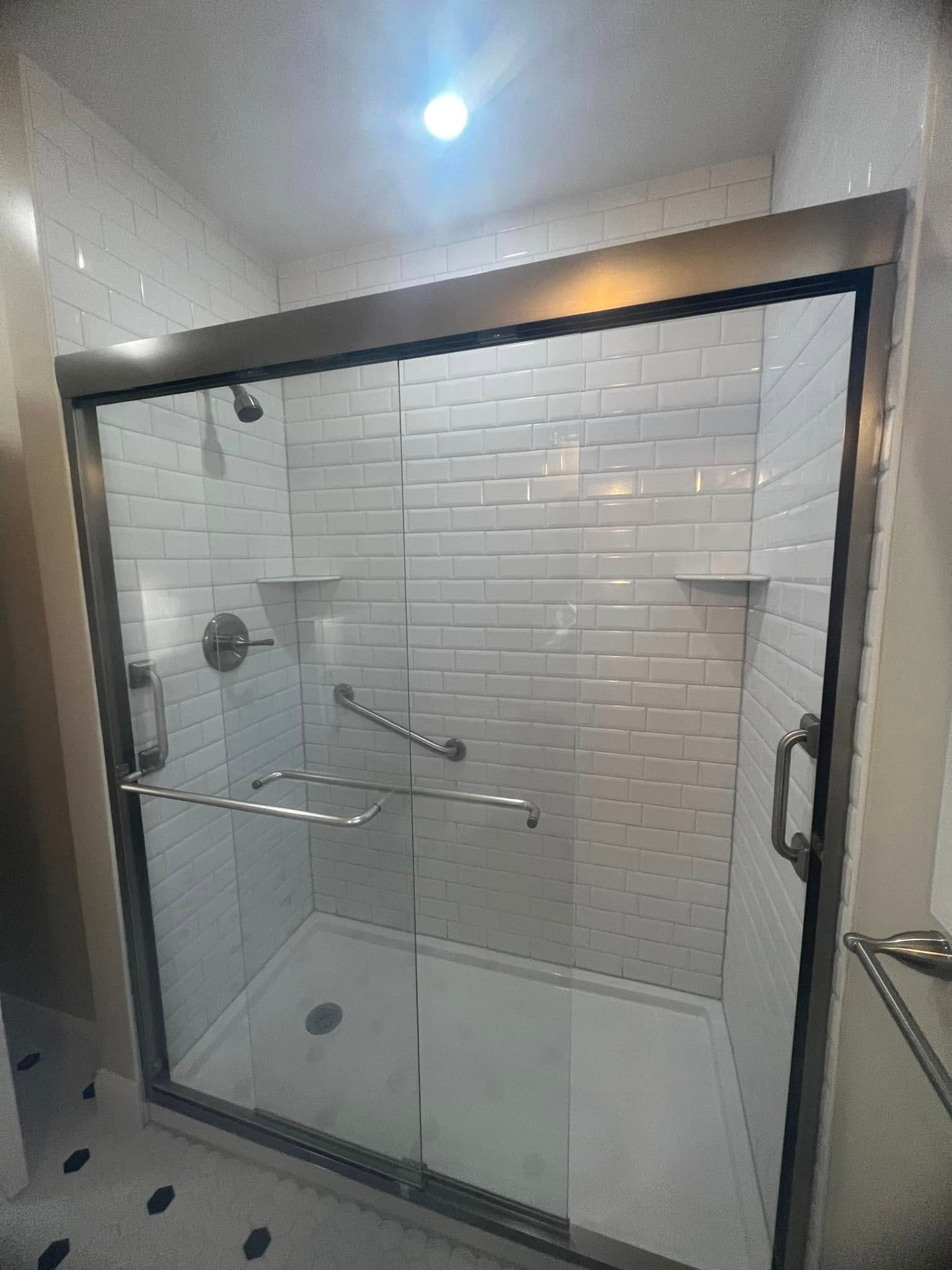A modern, white-tiled shower with a sliding glass door and grab bar.