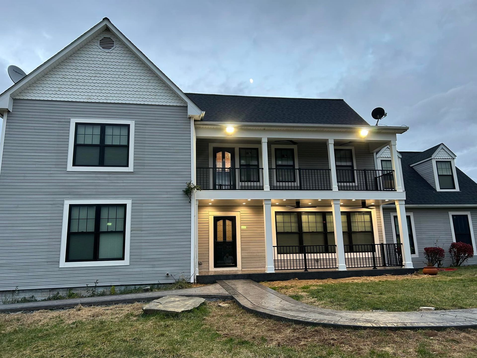 Two-story house with light gray siding, black trim, porch, and walkway; cloudy dusk sky.