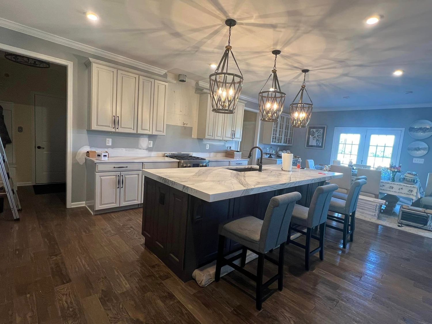 Kitchen with island, dark cabinets, white countertops, three pendant lights, and grey bar stools.